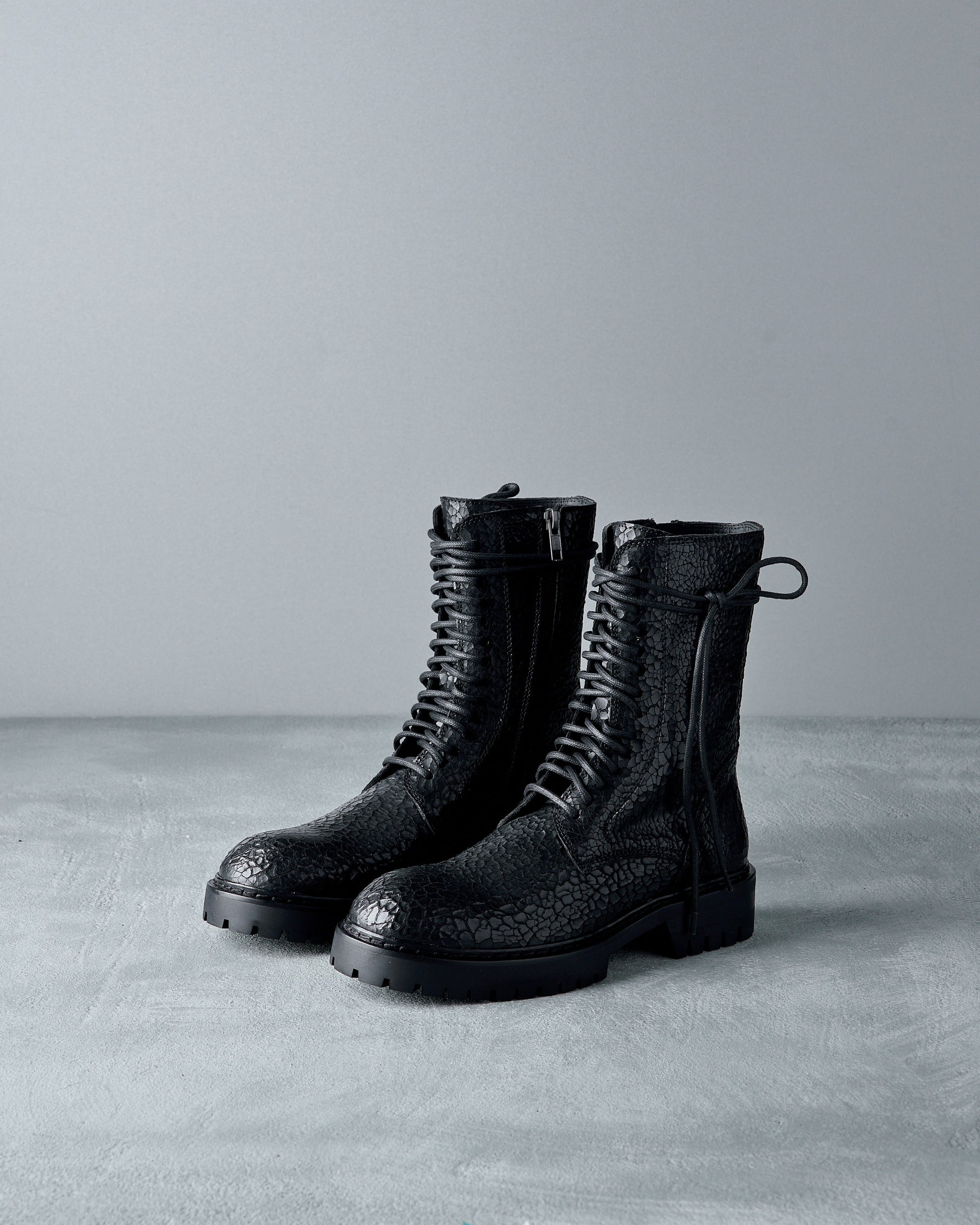 Pair of black lace-up Ann Demeulemeester boots on a gray surface with a gray background