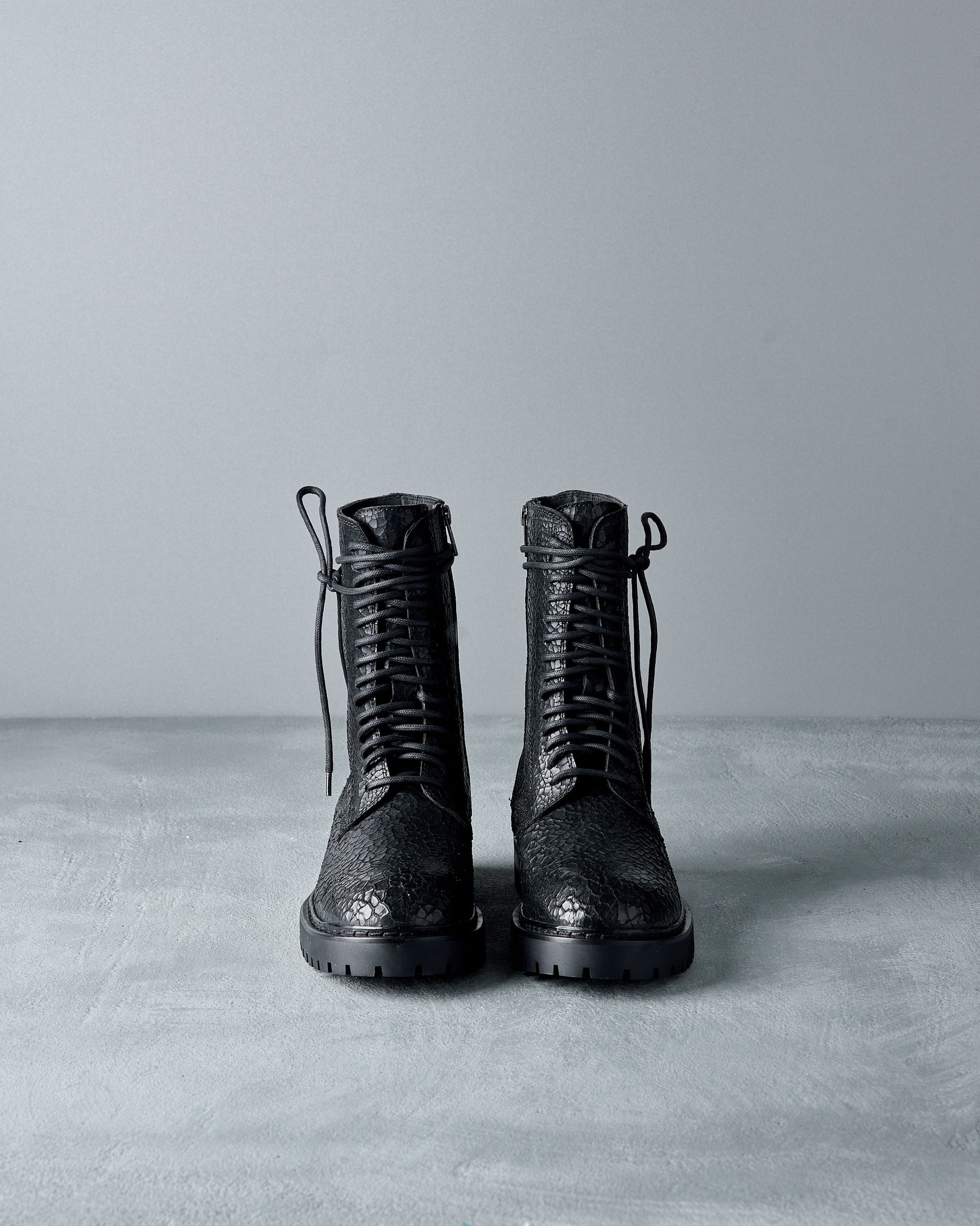 Pair of black leather Ann Demeulemeester  boots on a gray surface with a gray background