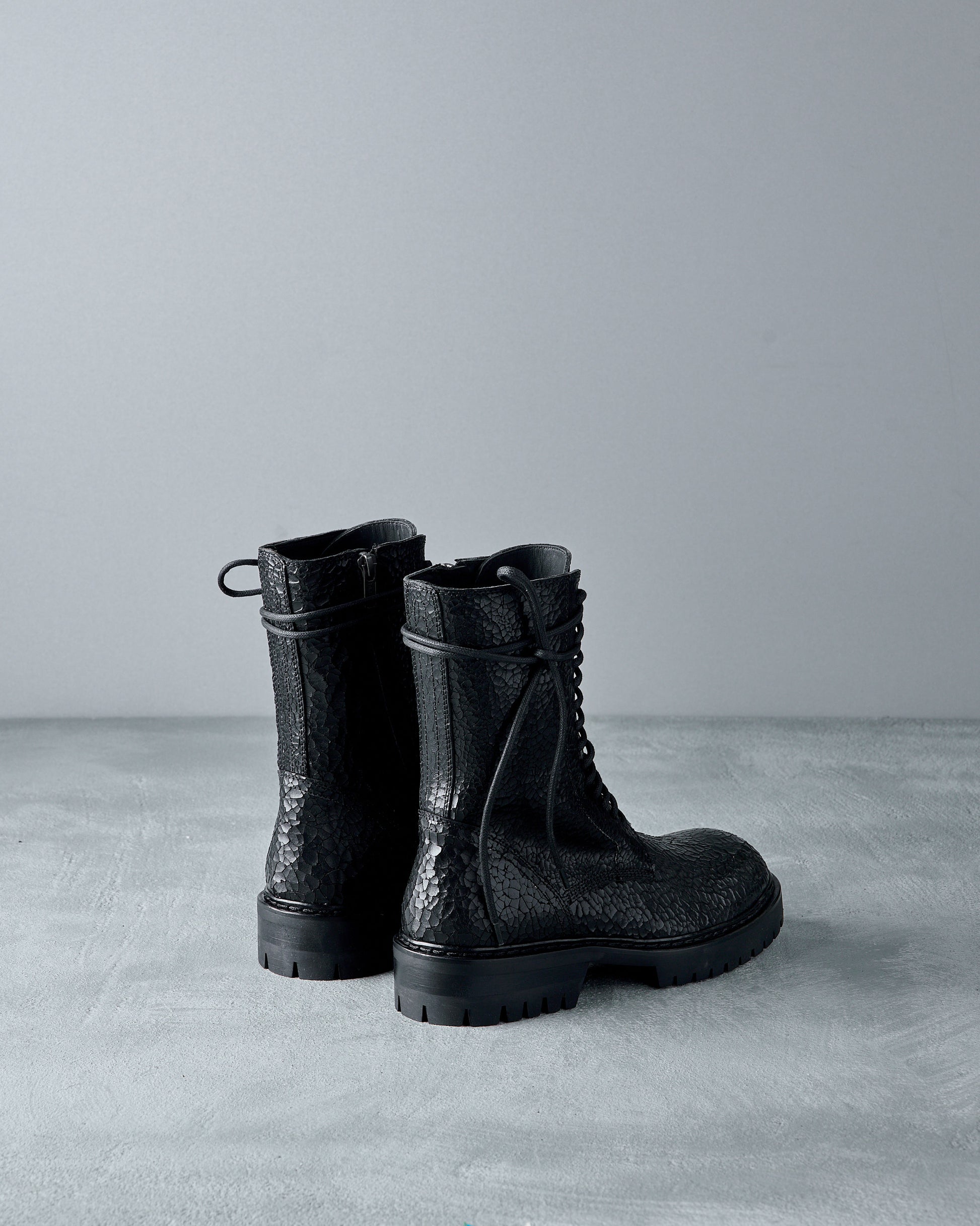 Pair of black textured Ann Demeulemeester boots on a gray surface with a gray background