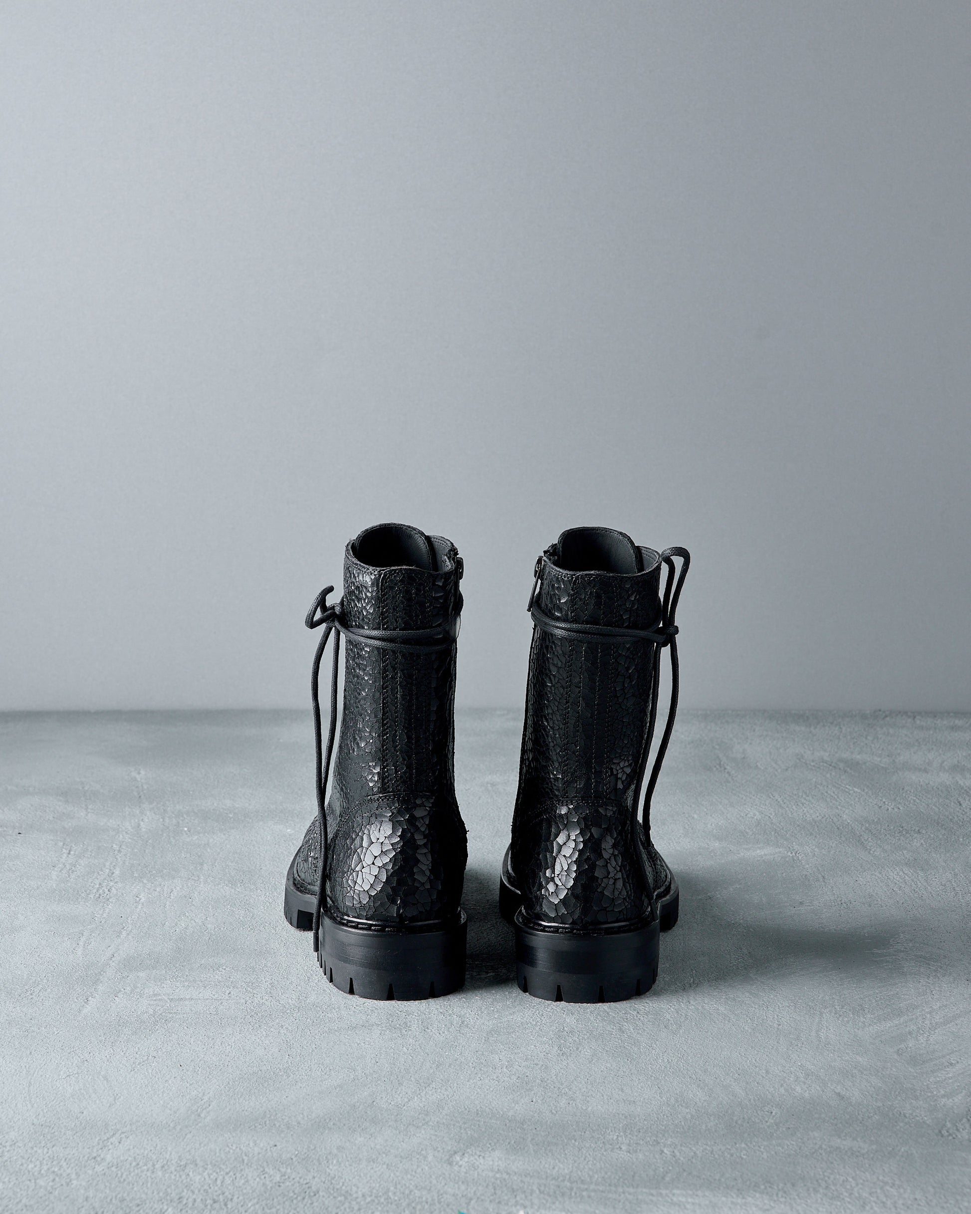 Pair of black Ann Demeulemeester  textured boots on a gray surface with a light gray background