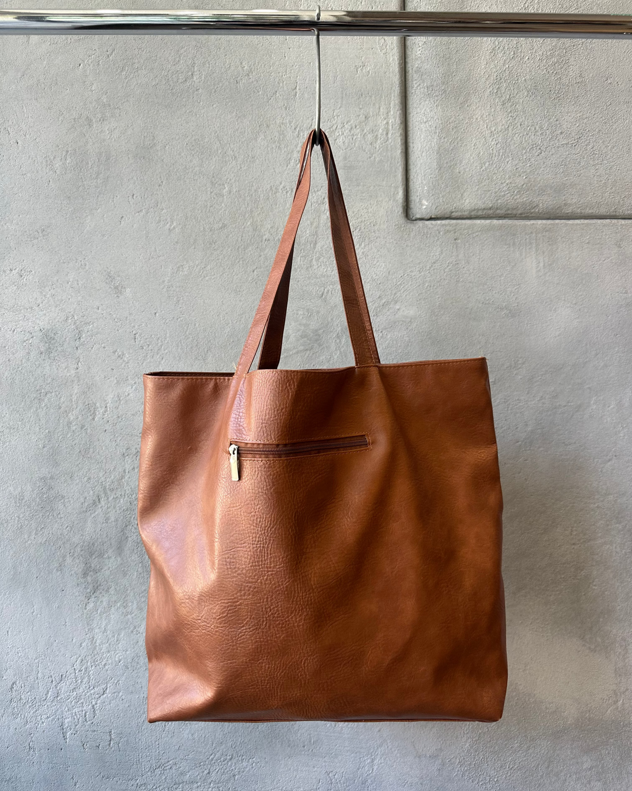 Brown tote bag with 'ANNE DEMEULEMEESTER' text hanging on a gray wall.