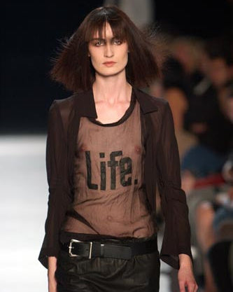 Model wearing a black Ann Demeulemeester shirt with 'Life.' printed on it at a fashion show.