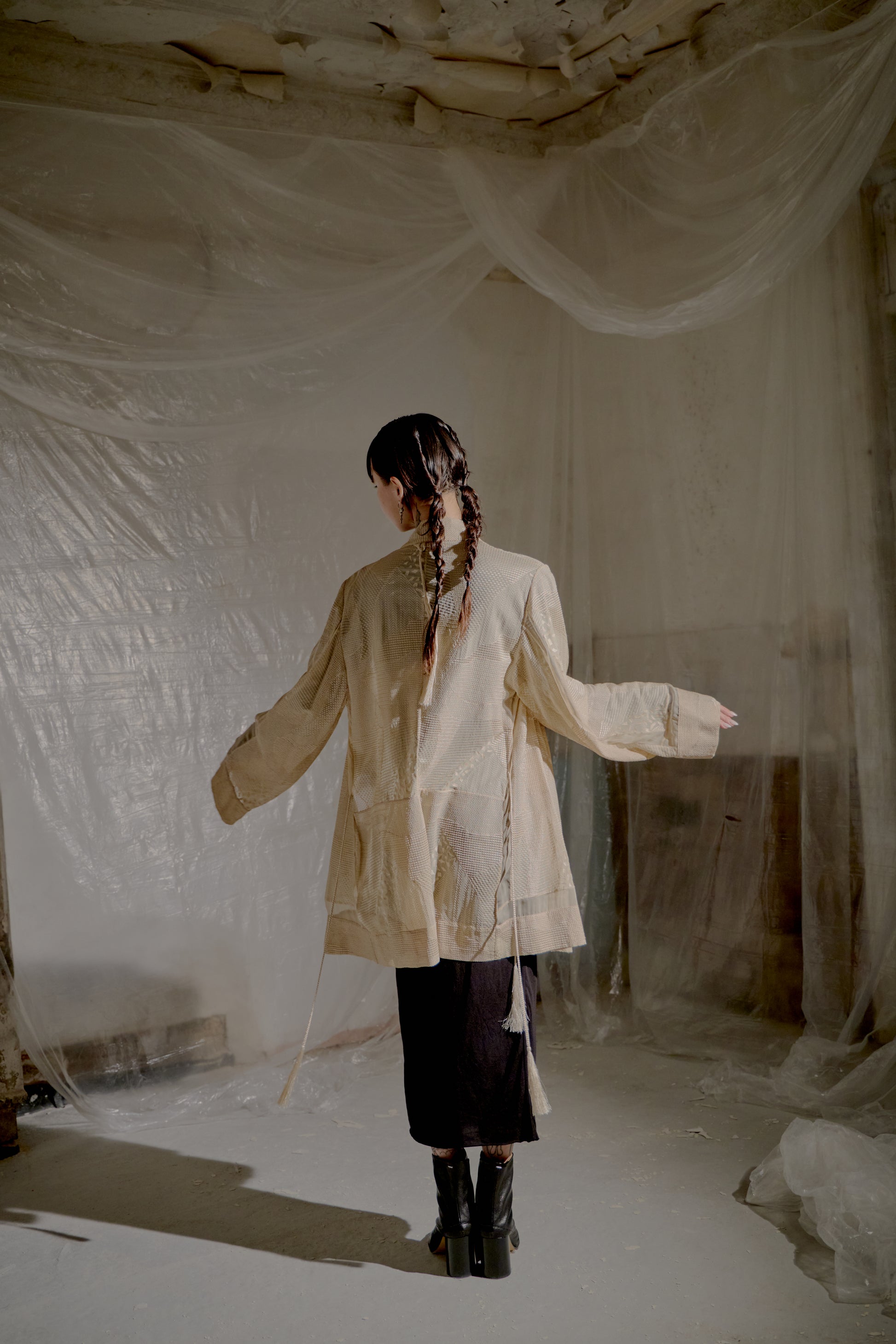 Person standing in a room with white fabric walls and floor, wearing a light-coloured Ann Demeulemeester coat.