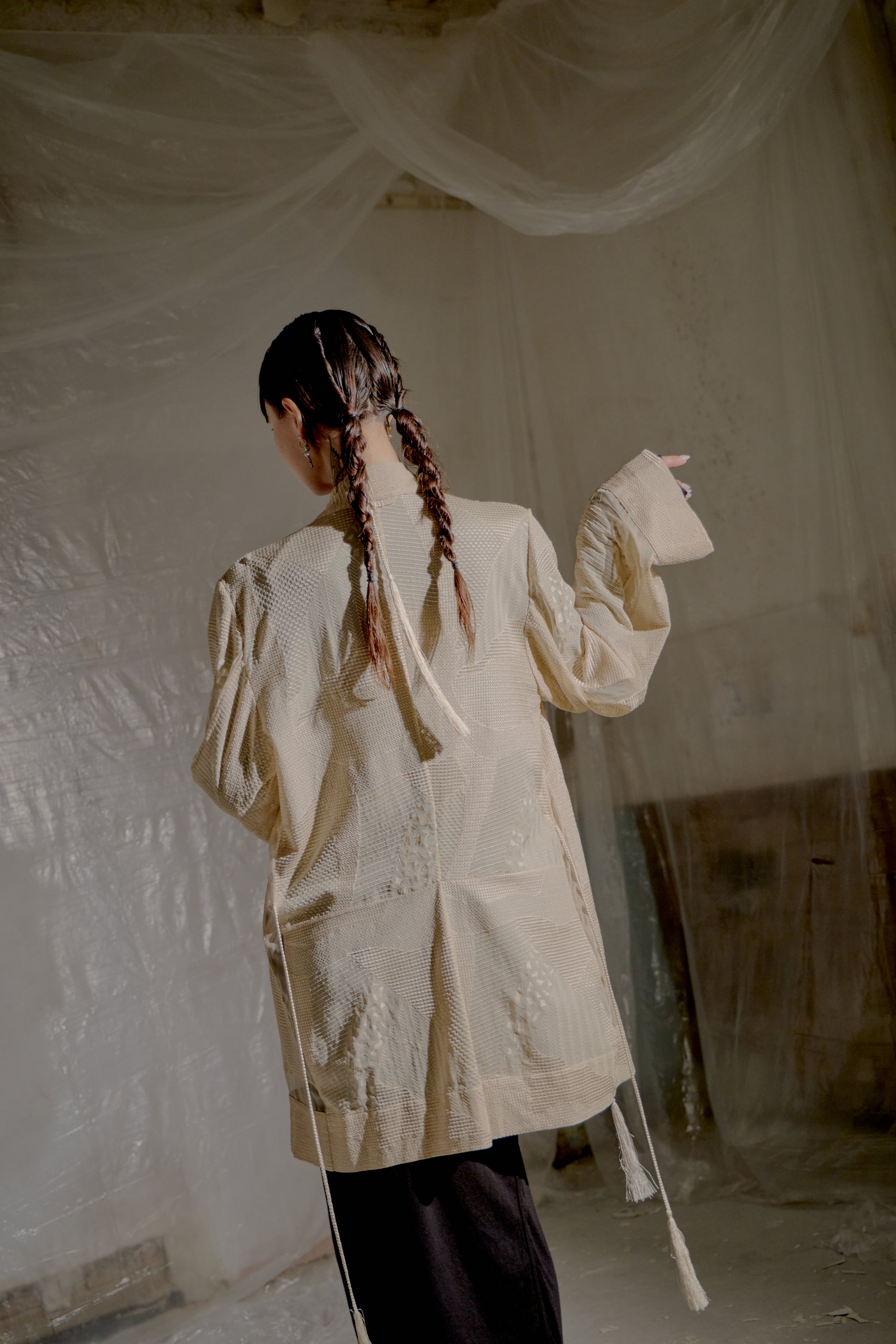 Person wearing a beige Ann Demeulemeester coat with braided hair in a minimal indoor setting