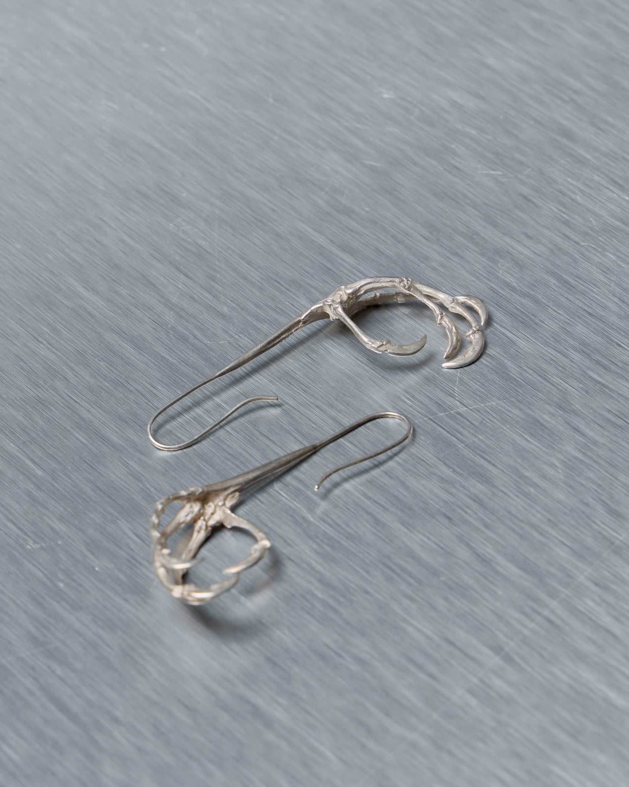 Pair of silver Ann Demeulemeester earrings on a gray background