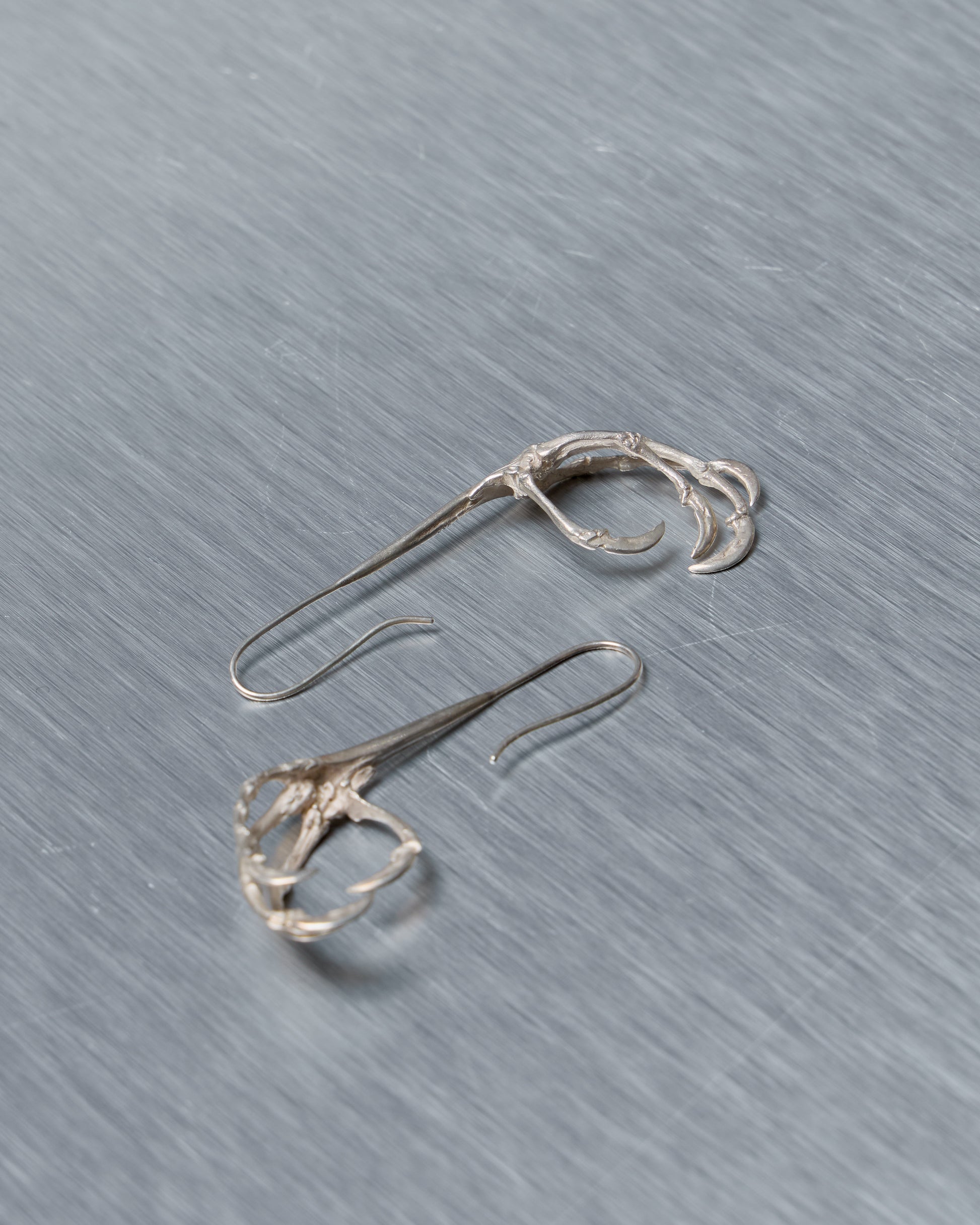 Pair of silver Ann Demeulemeester earrings on a textured gray surface