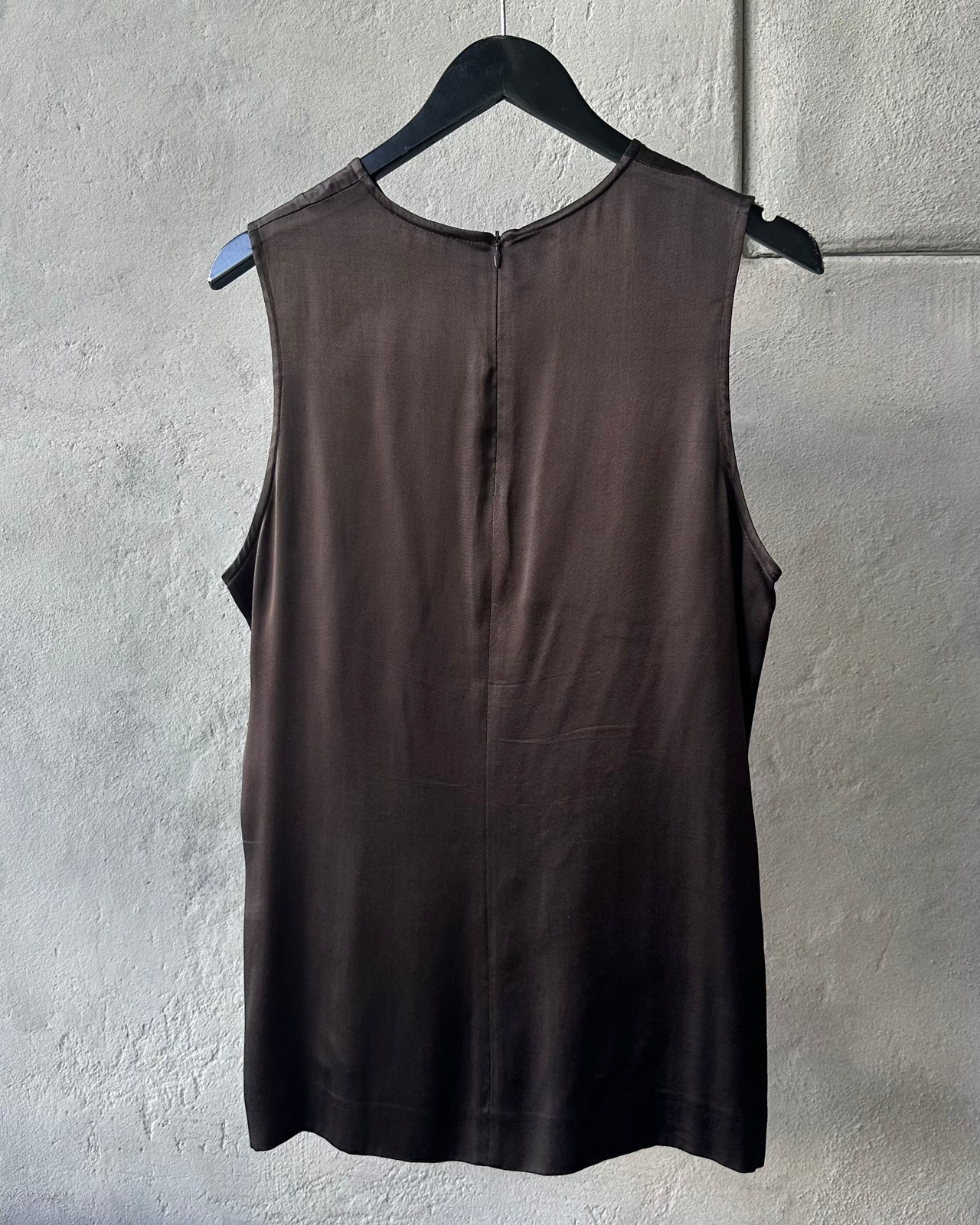 Brown sleeveless Ann Demeulemeester shirt on a hanger against a gray wall