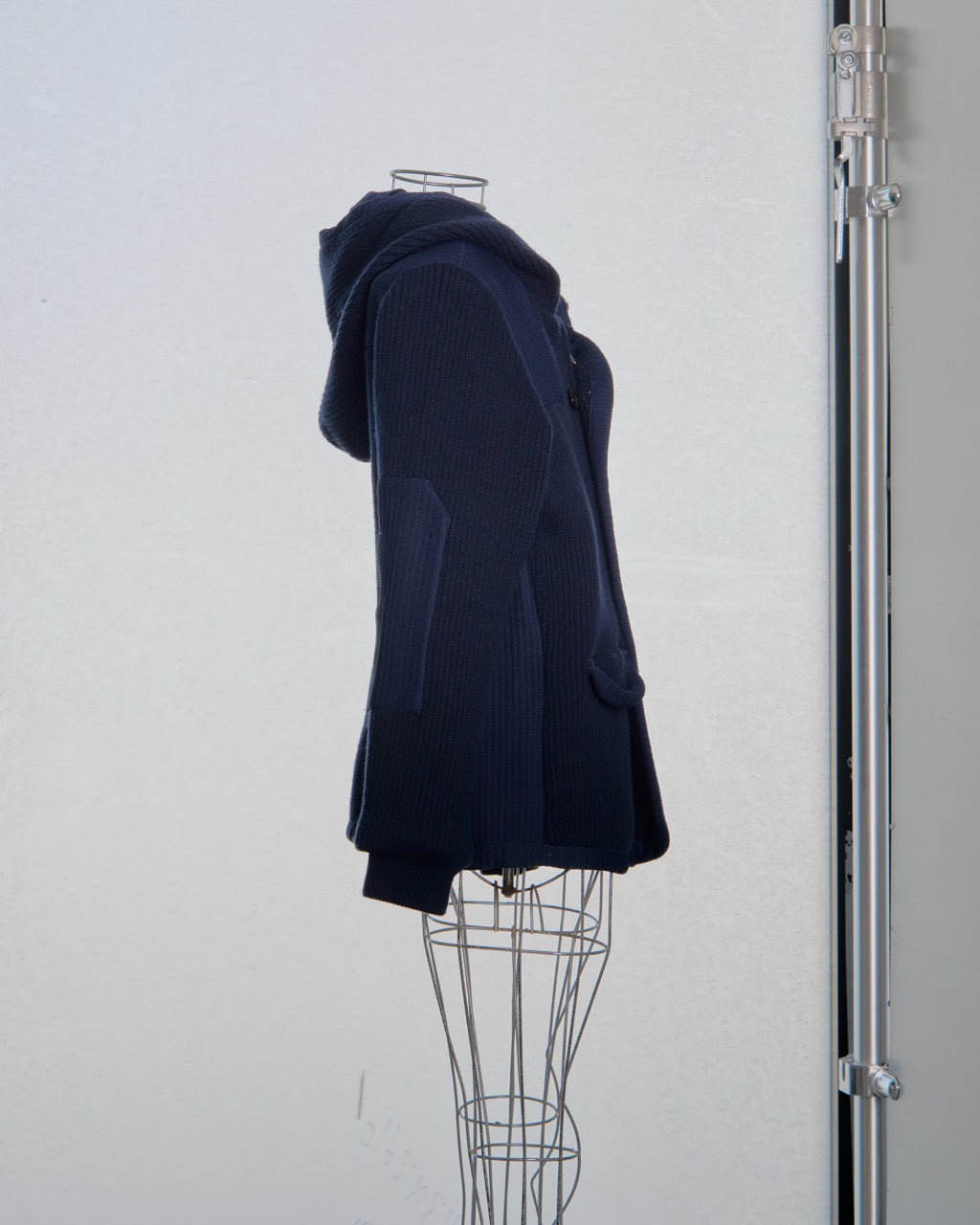 Navy blue Balenciaga hooded coat on a mannequin against a white wall