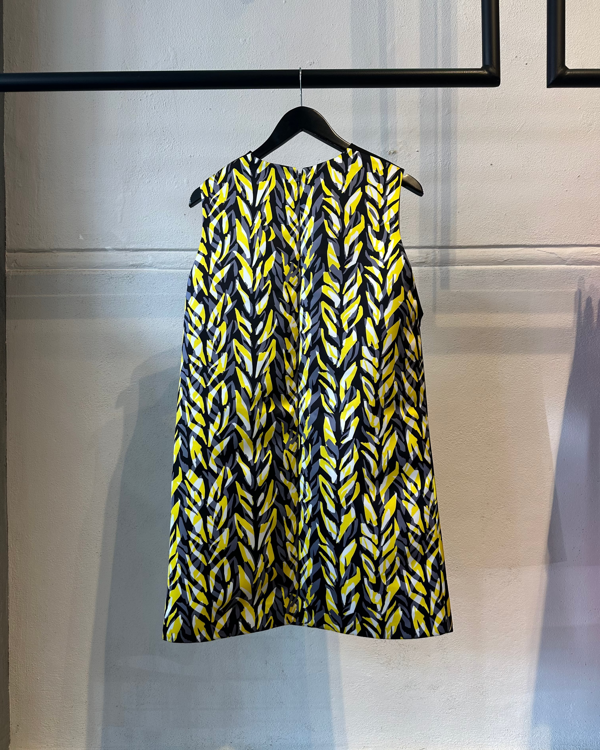 Yellow and black patterned Balenciaga dress on a hanger against a white wall.