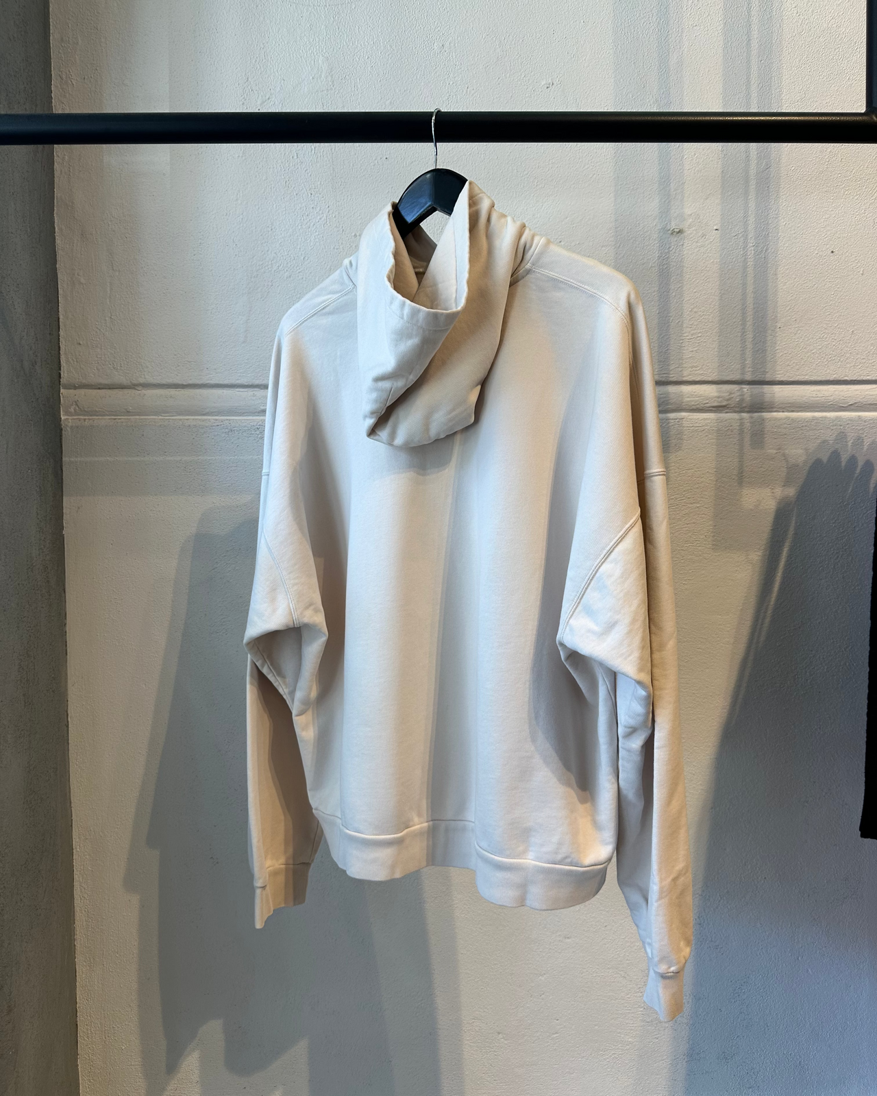 White hoodie with Balenciaga logo on a hanger against a neutral background