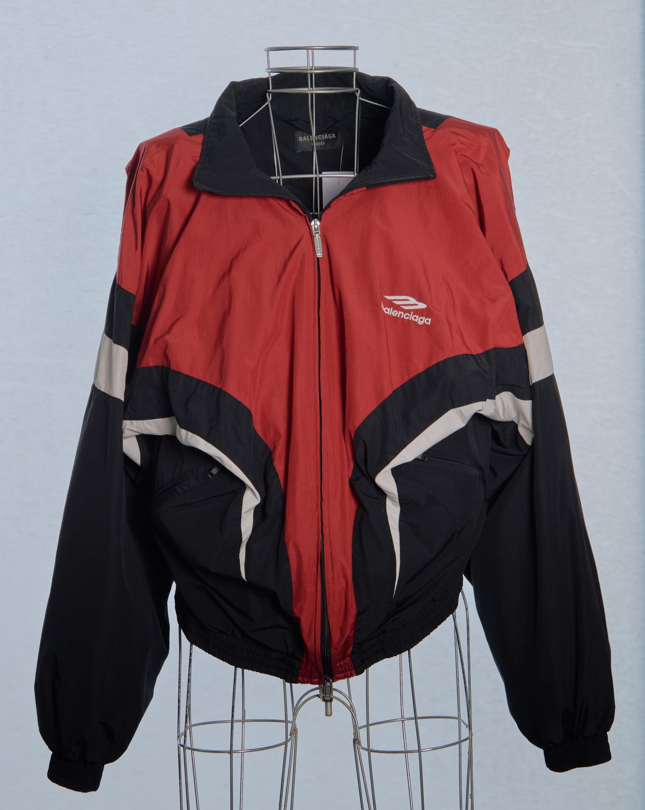 Red and black Balenciaga jacket with a logo on a mannequin against a light blue background