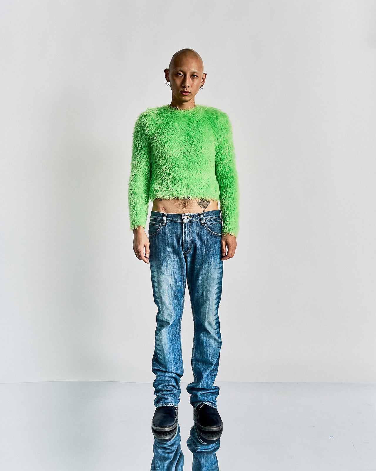 Person wearing a bright green fuzzy Balenciaga sweater and blue jeans on a white background