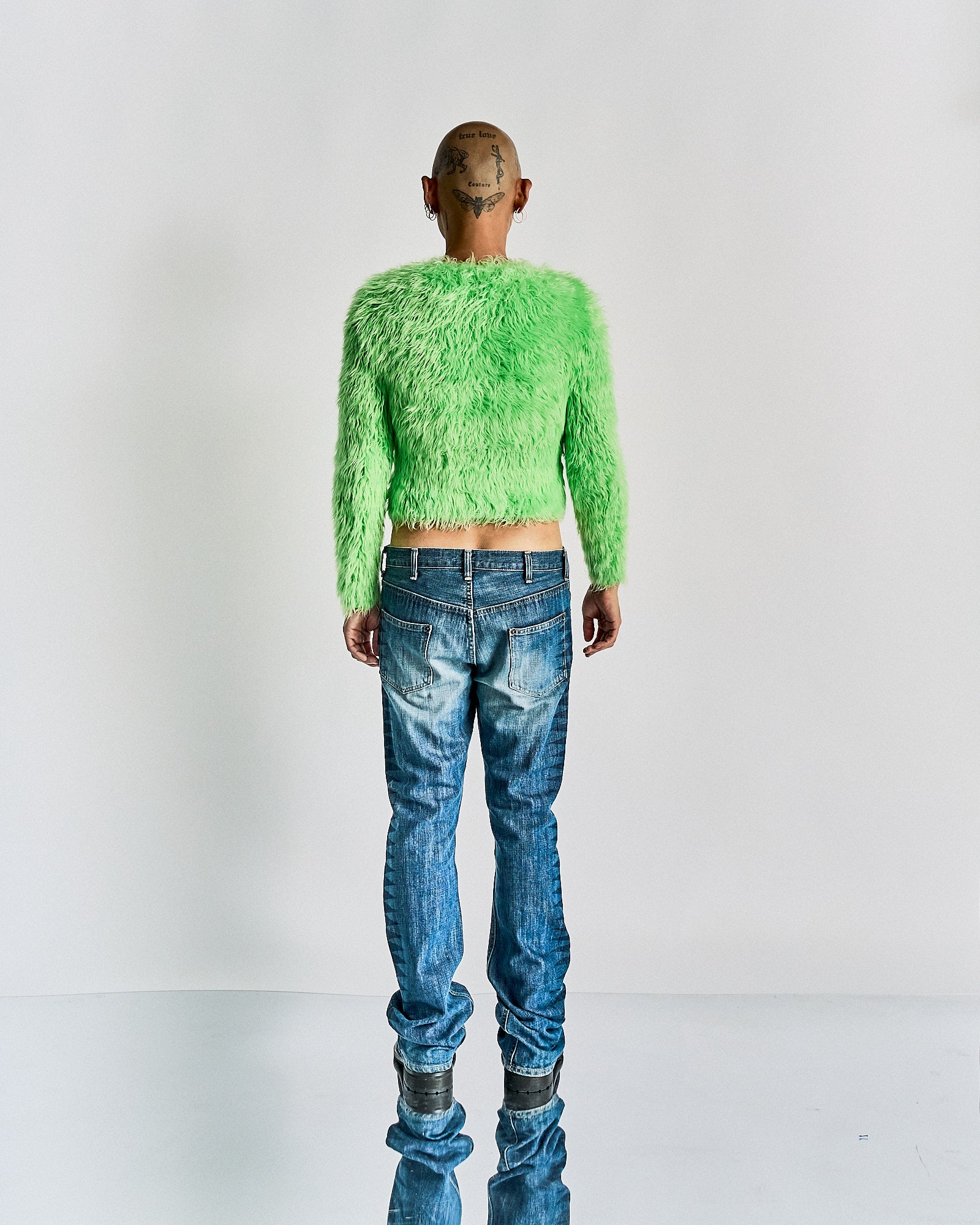 Person wearing a bright green fuzzy Balenciaga sweater and blue jeans on a white background