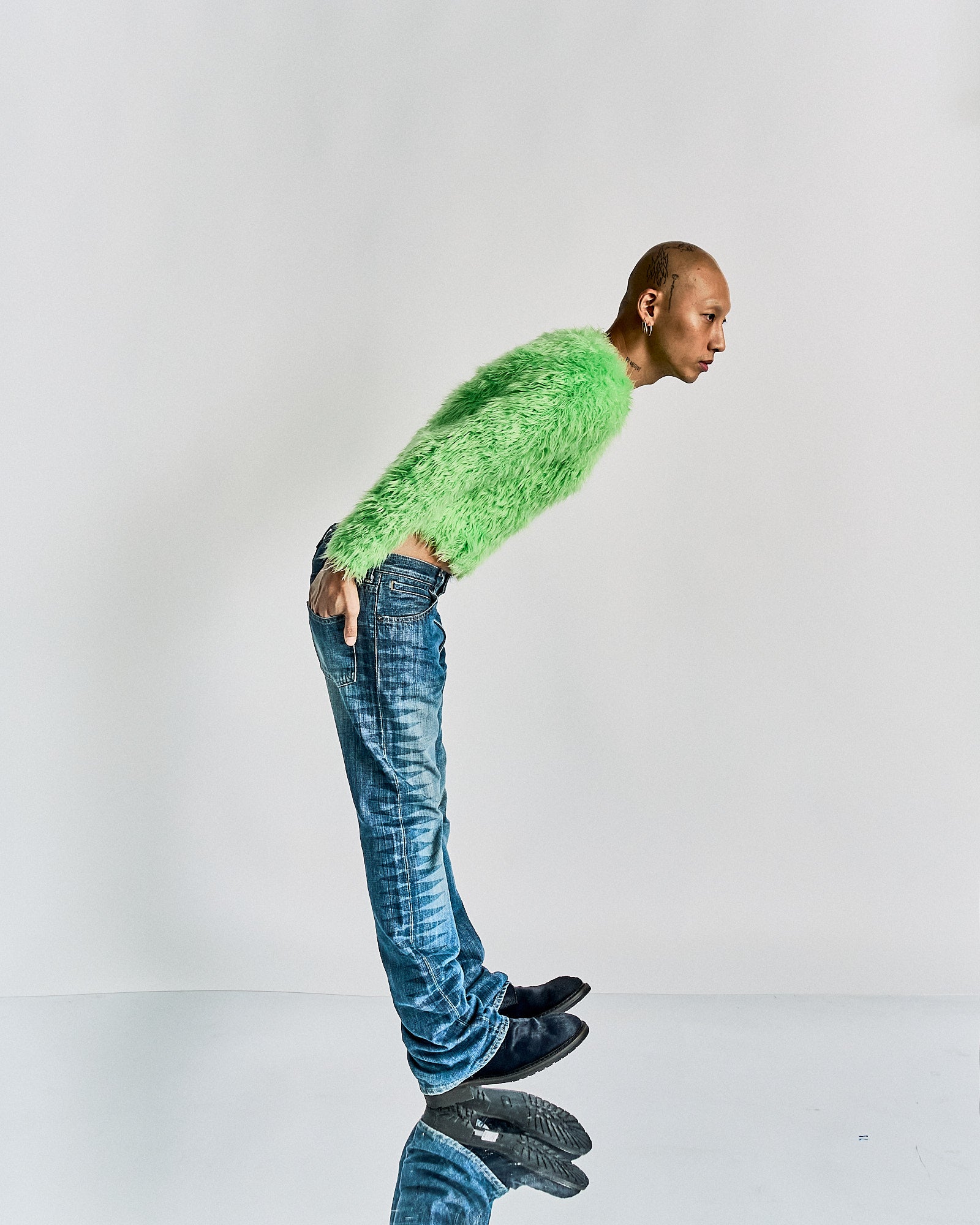 Person wearing a bright green faux fur Balenciaga jumper and blue jeans on a white background