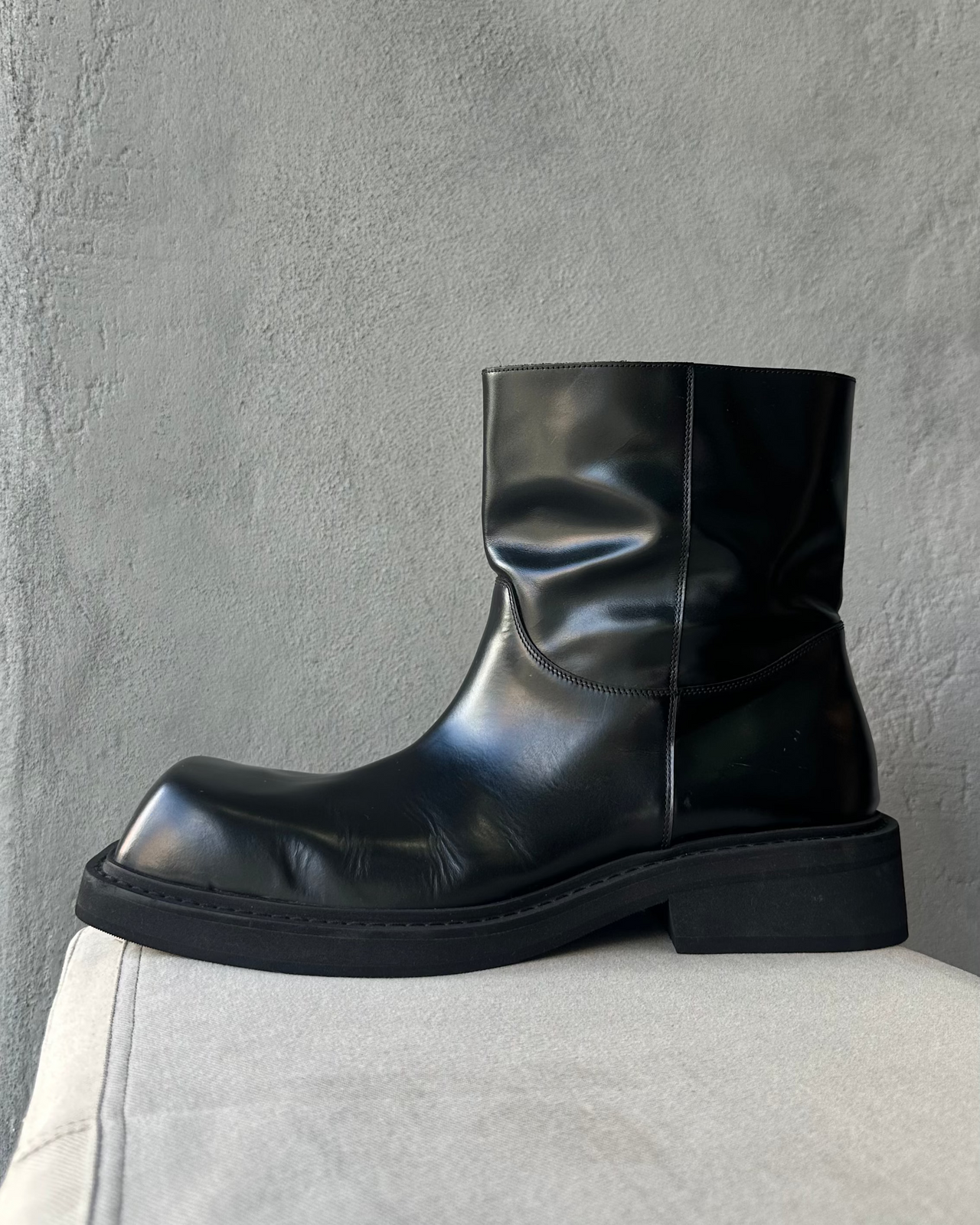Black leather boot on a light gray surface with a concrete wall background