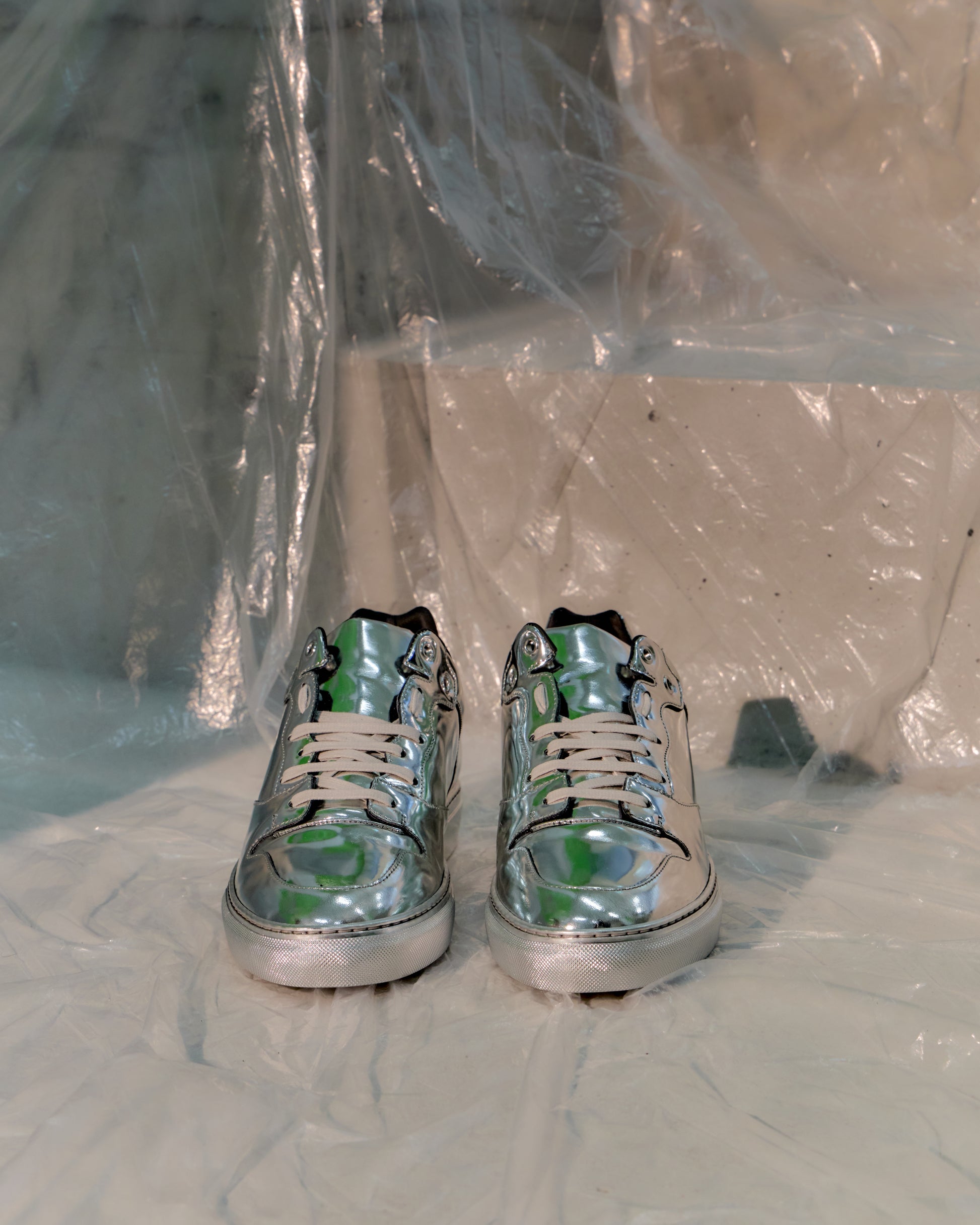 Silver Balenciaga high-top sneakers on a white surface with a clear plastic sheet in the background