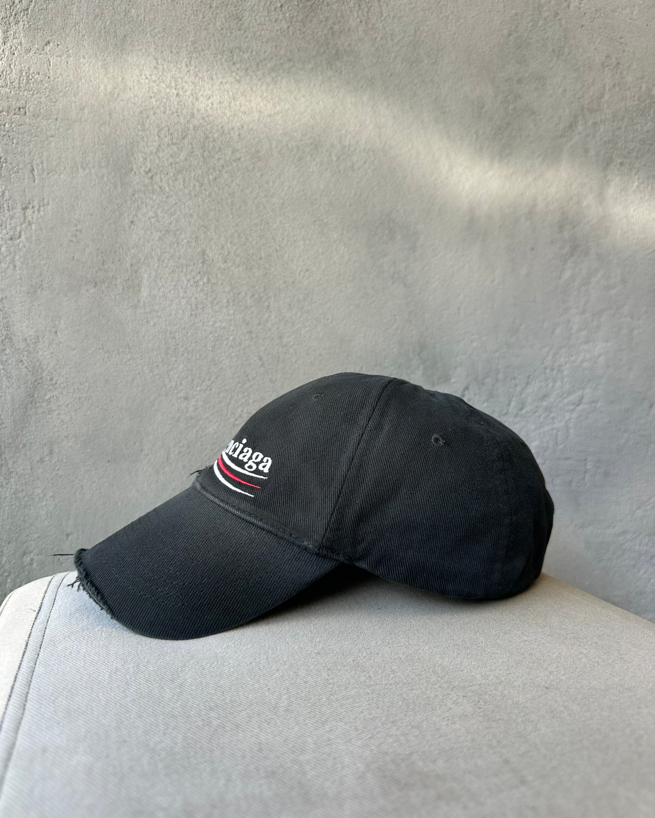 Black Balenciaga cap on a light gray surface with a textured gray wall background
