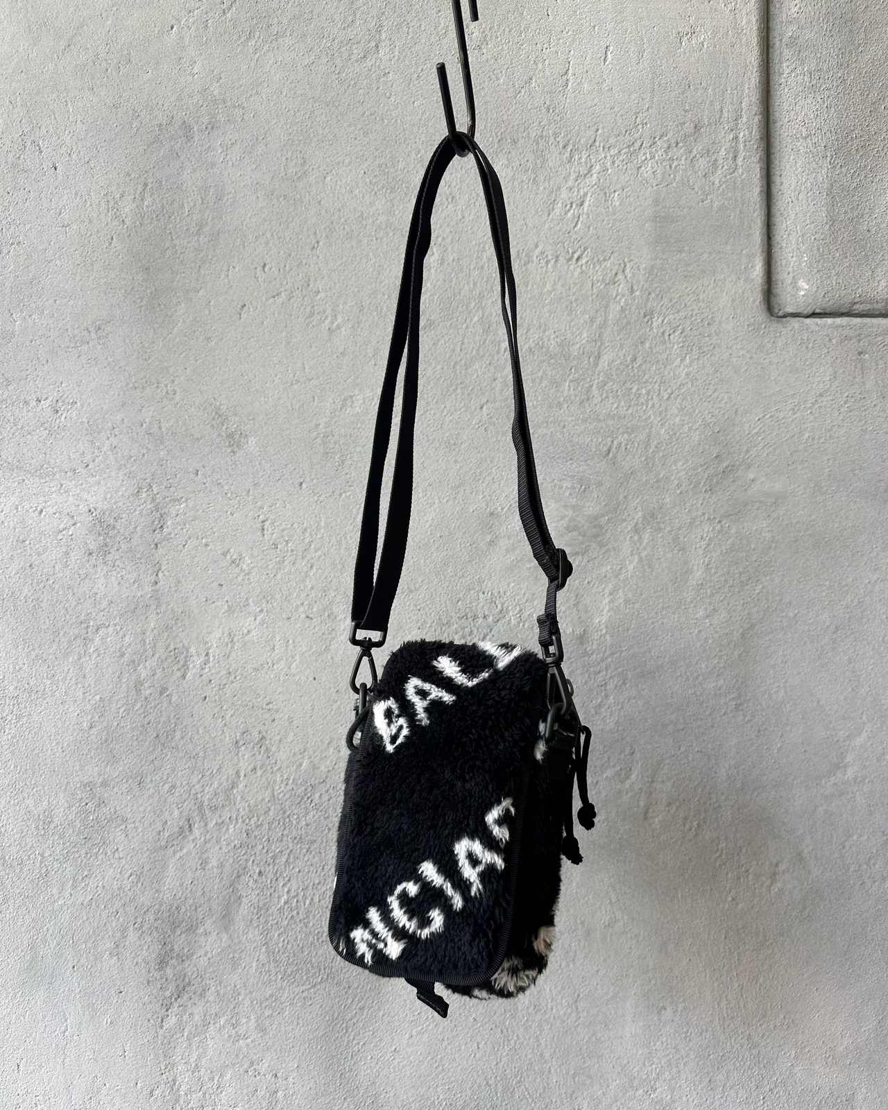 Small black Balenciaga bag with white text on a textured gray wall