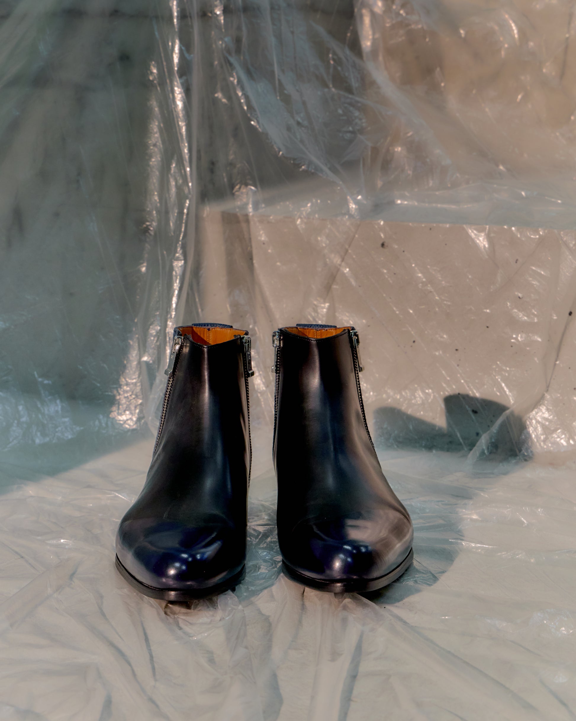 Pair of black leather Balenciaga boots on a reflective surface with plastic sheeting in the background