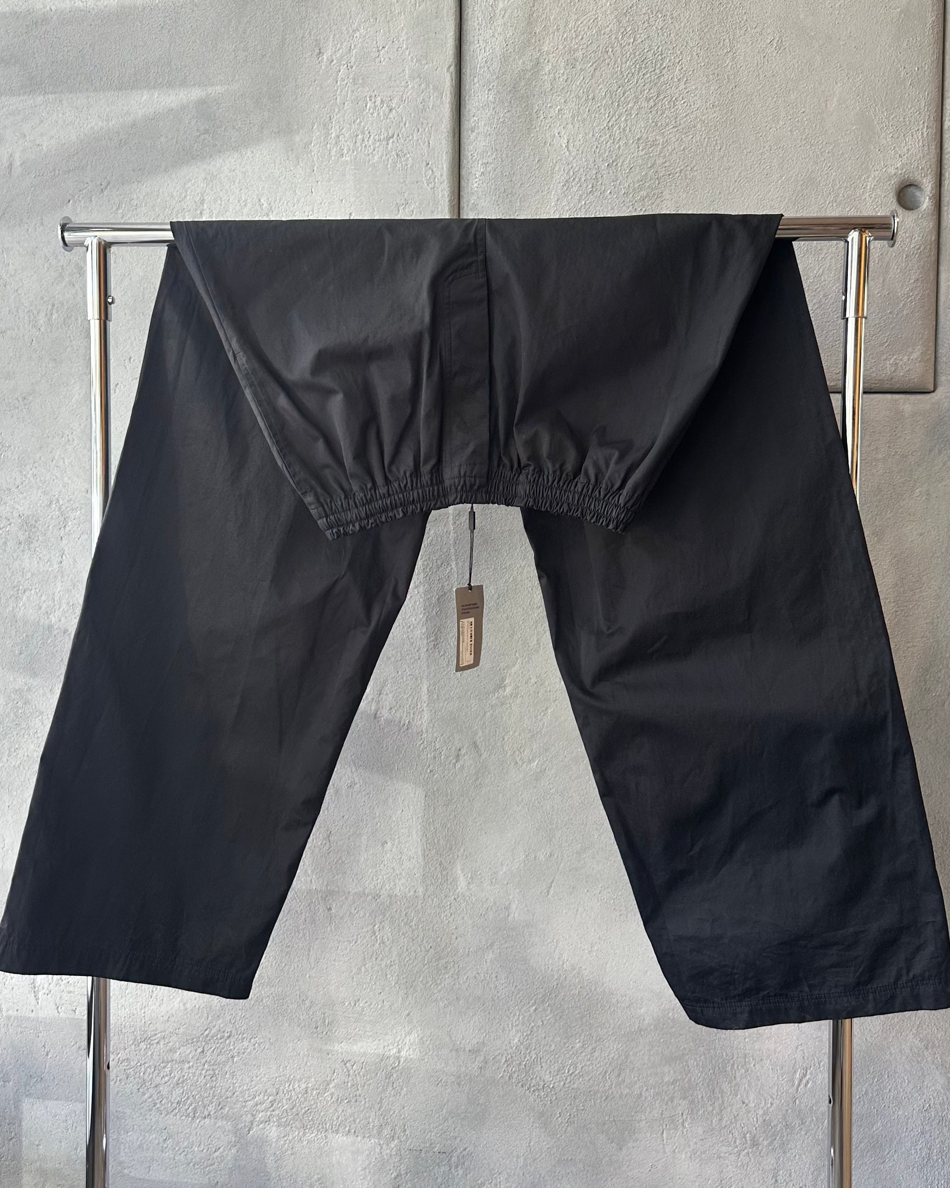 Black Balenciaga pants hanging on a metal rack against a gray wall.