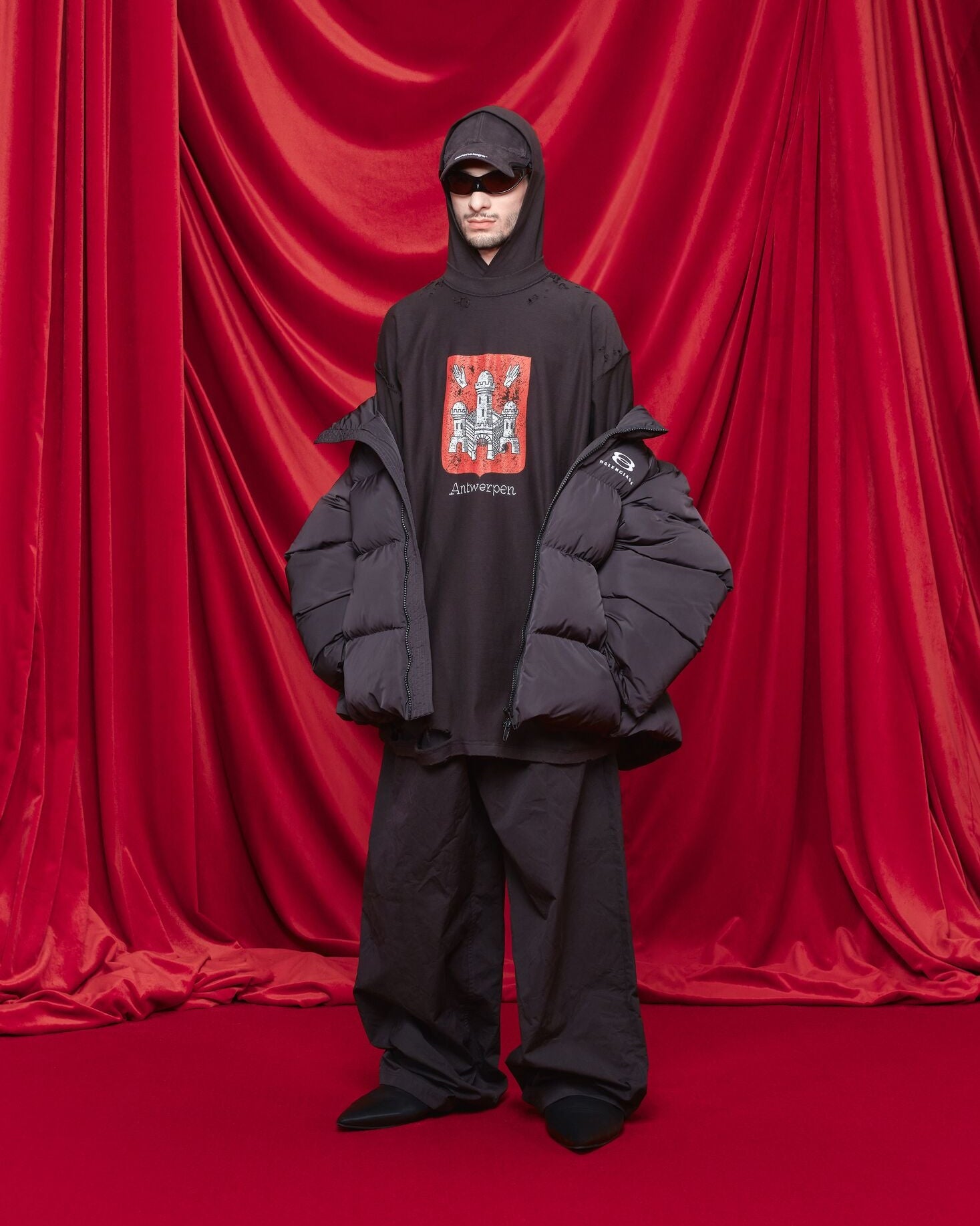 Person wearing a black Balenciaga outfit with a graphic design in front of red curtains
