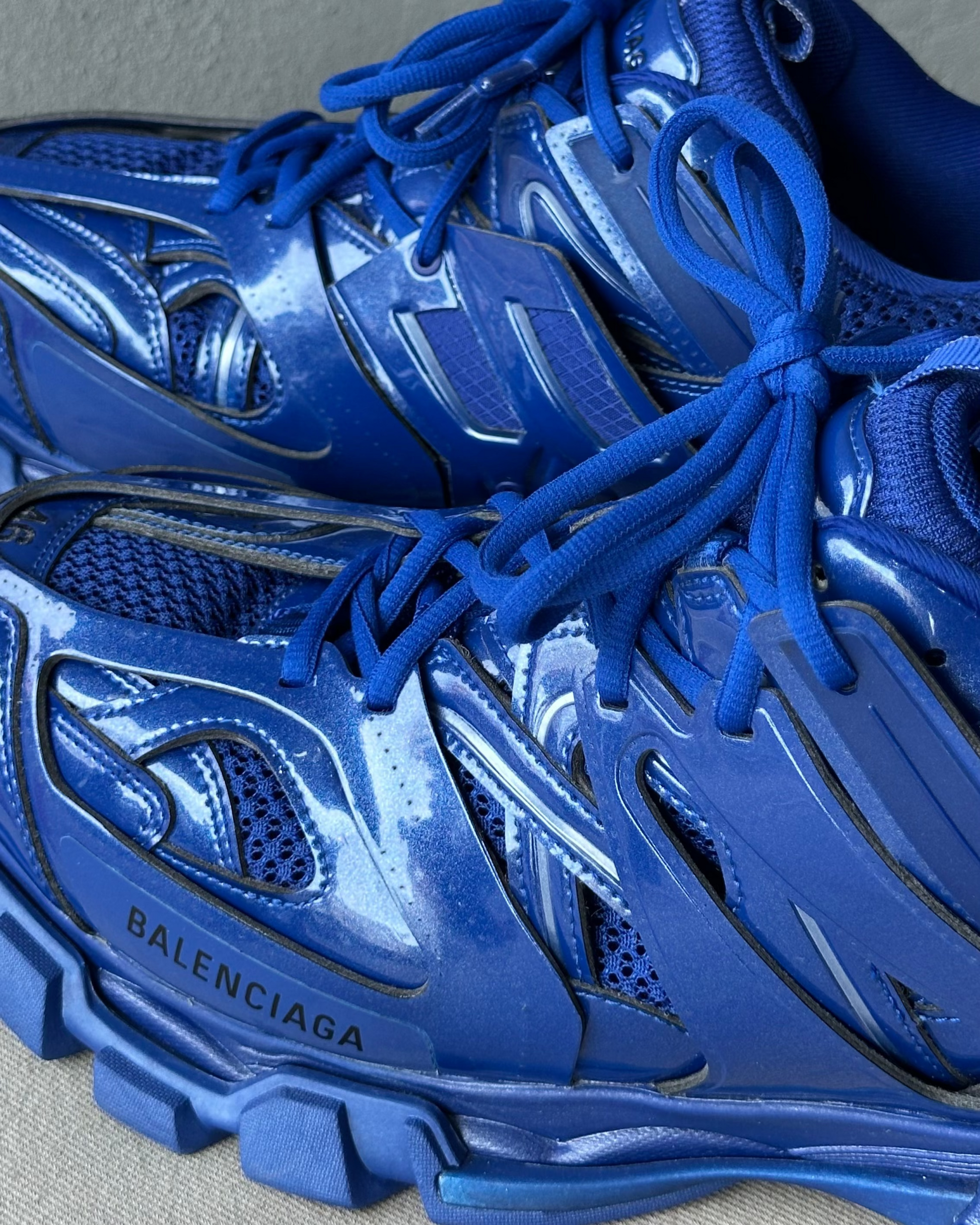 Blue Balenciaga sneakers with reflective material on a gray background