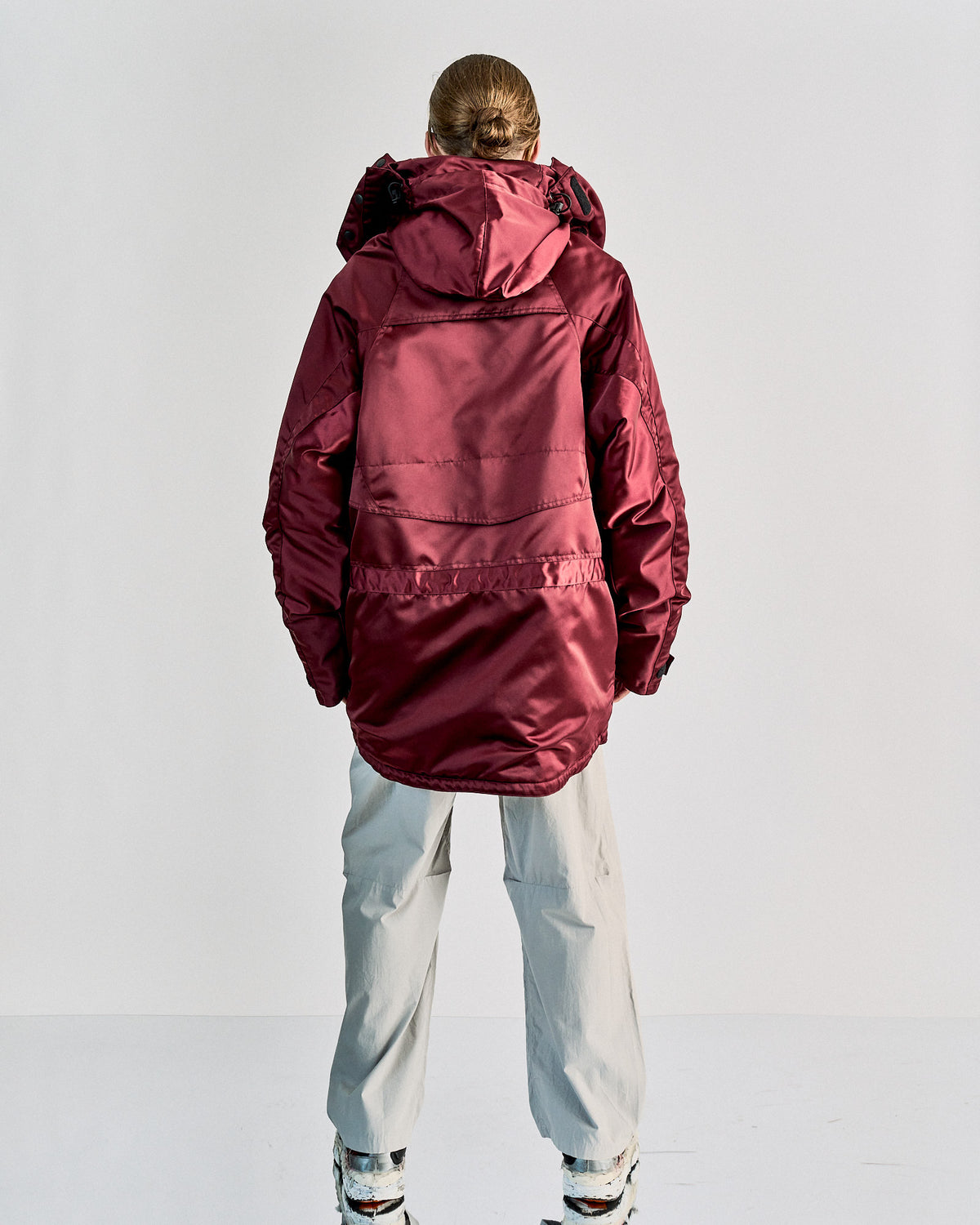 A model in a deep burgundy hooded Balenciaga parka walks confidently against a black background, exuding a sleek and modern winter style.