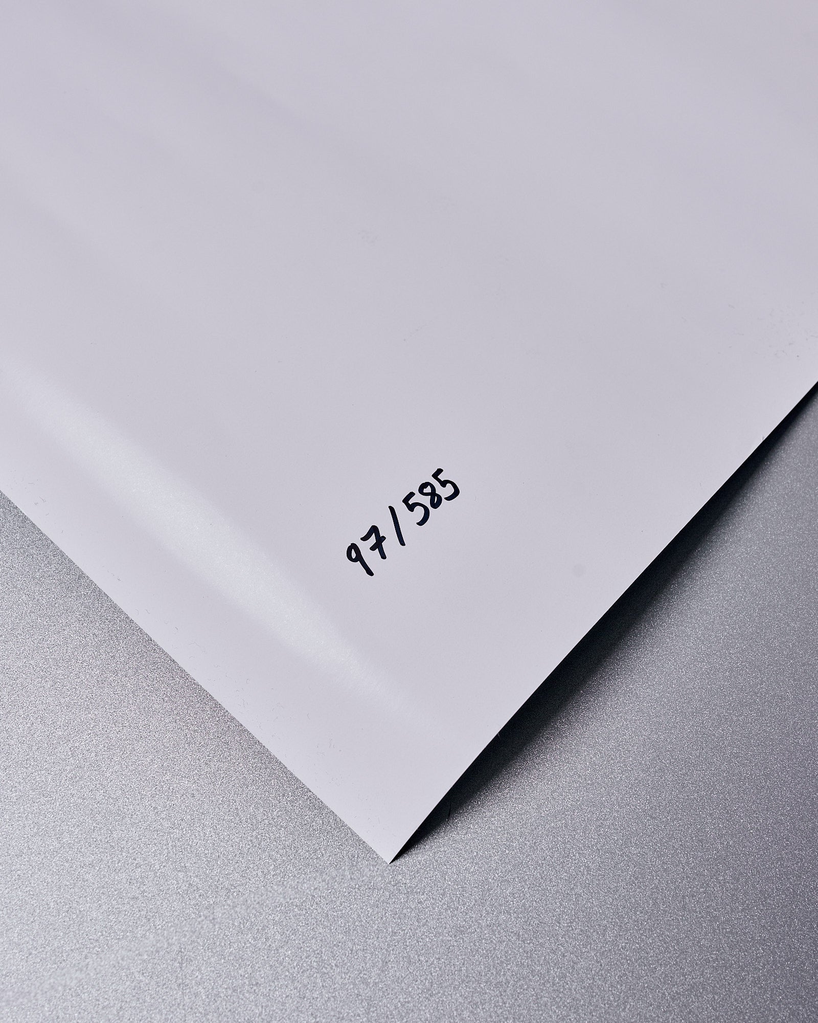 Close-up of a glossy white sheet corner from a Balenciaga x Cardi B on a grey surface, marked with "97/585" in black. The image conveys a sense of minimalism and exclusivity.