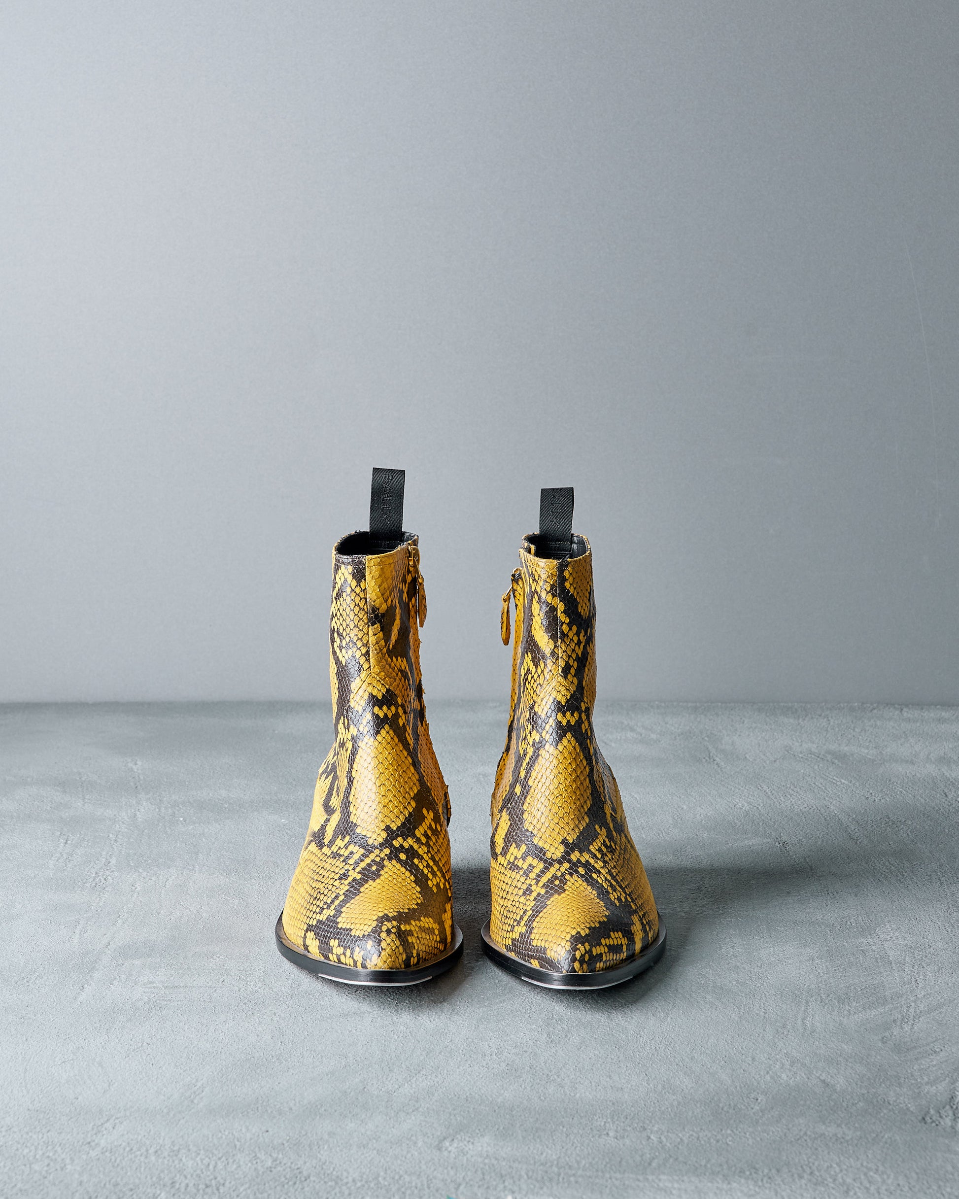 Pair of yellow Bally snake print boots on a gray background