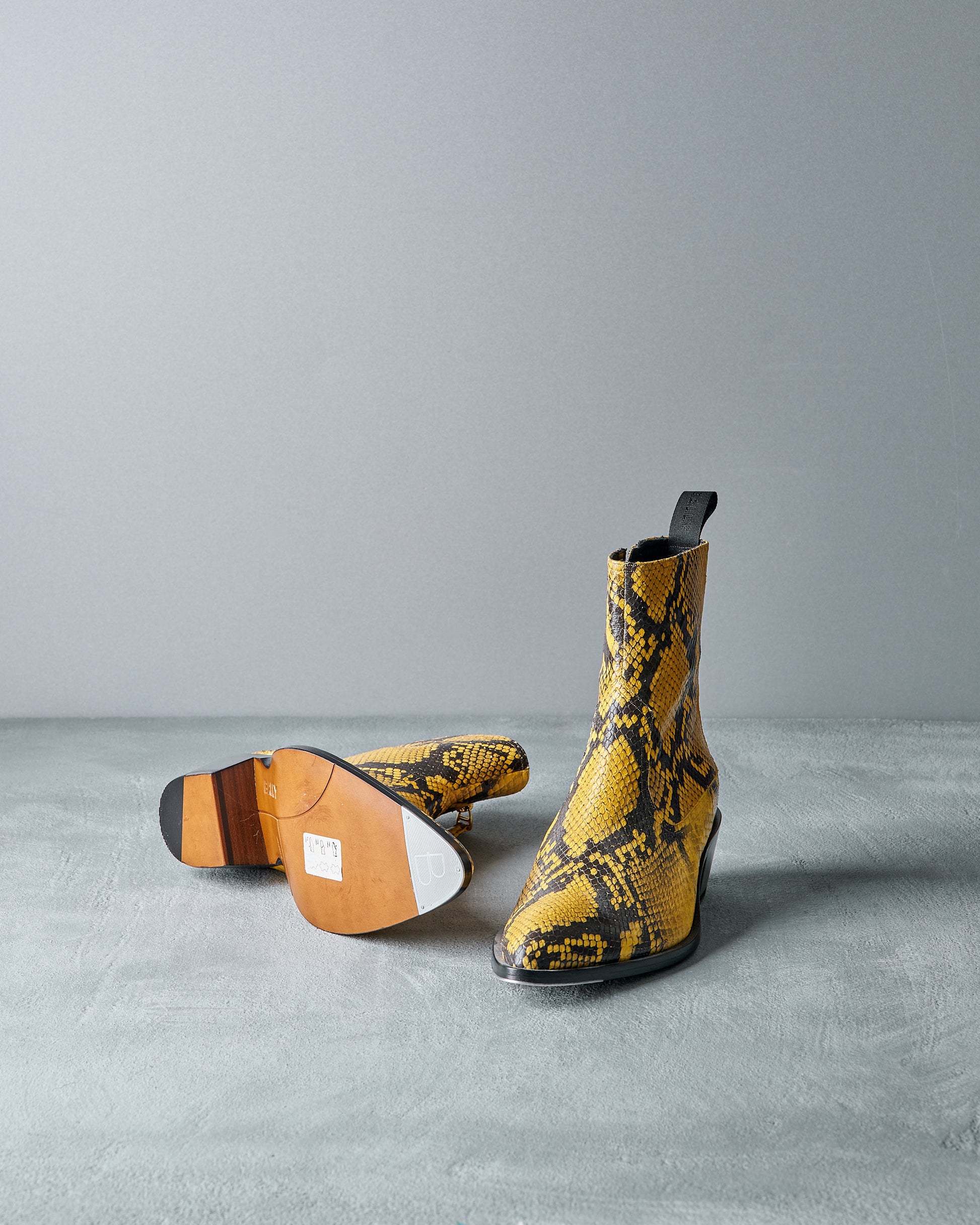 Yellow Bally snake-patterned boots on a gray surface with a gray background