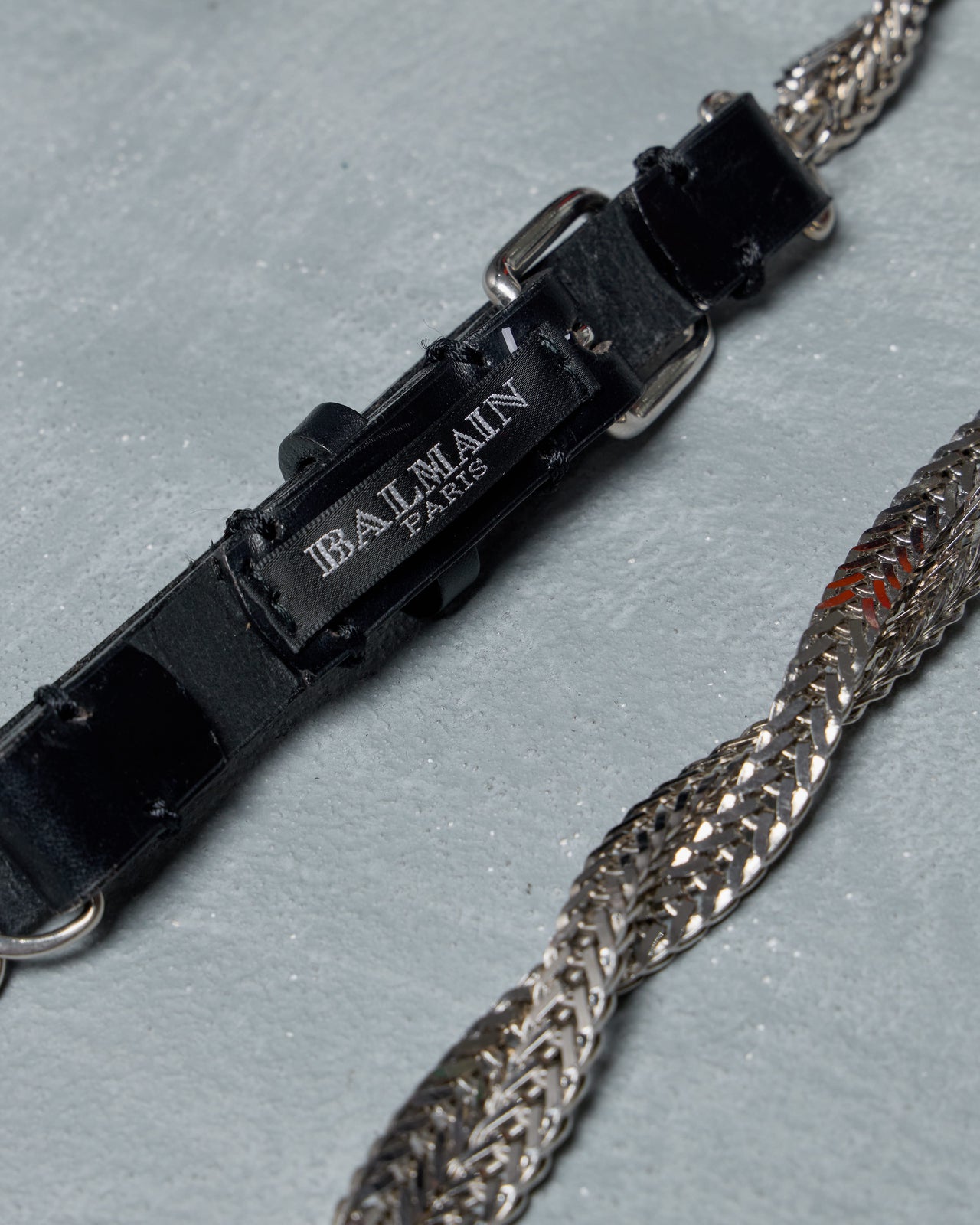 Silver Balmain chain belt with a black leather strap and buckle on a light gray background