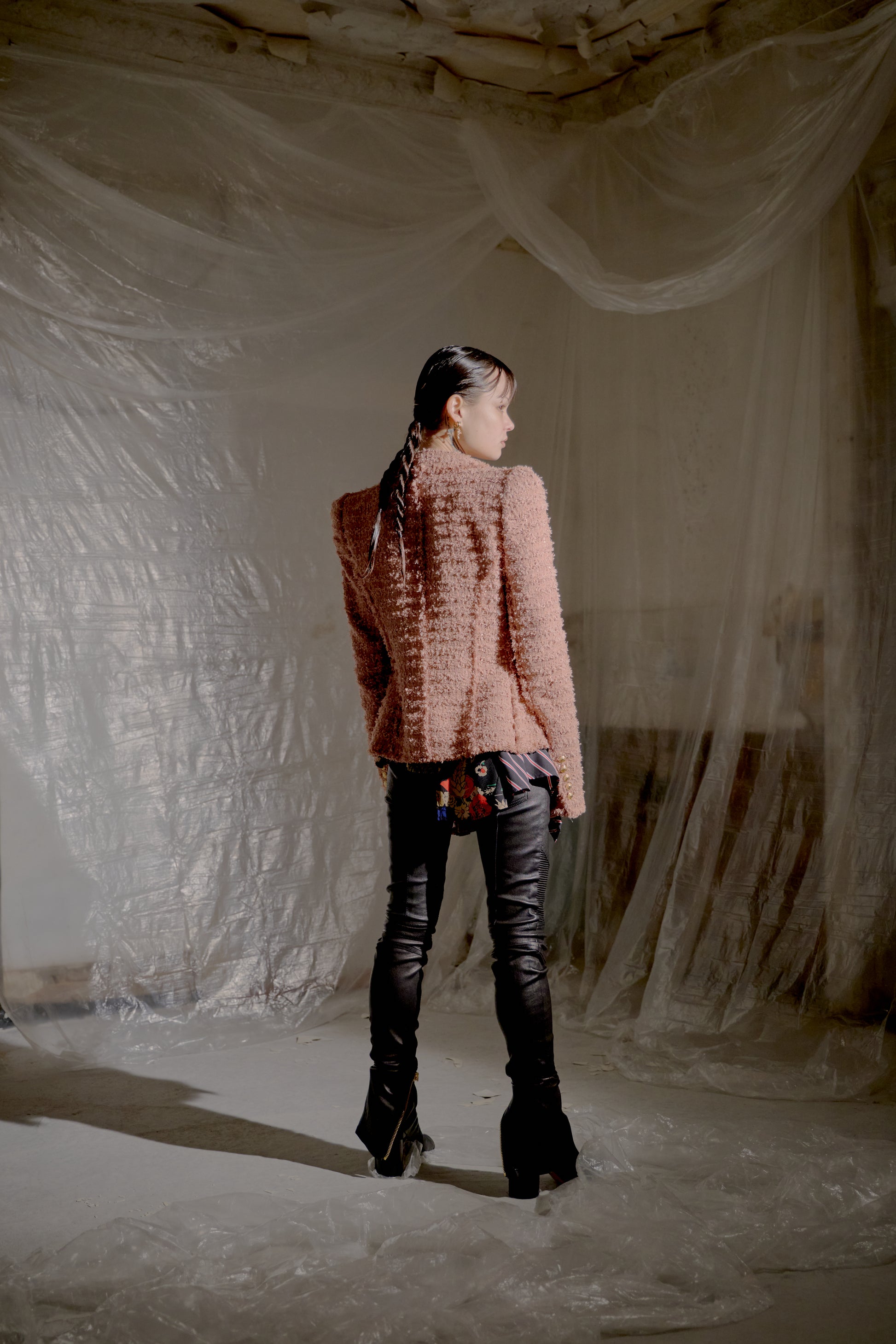 Person wearing a textured pink Balmain jacket and black pants standing in a room with white plastic sheeting.