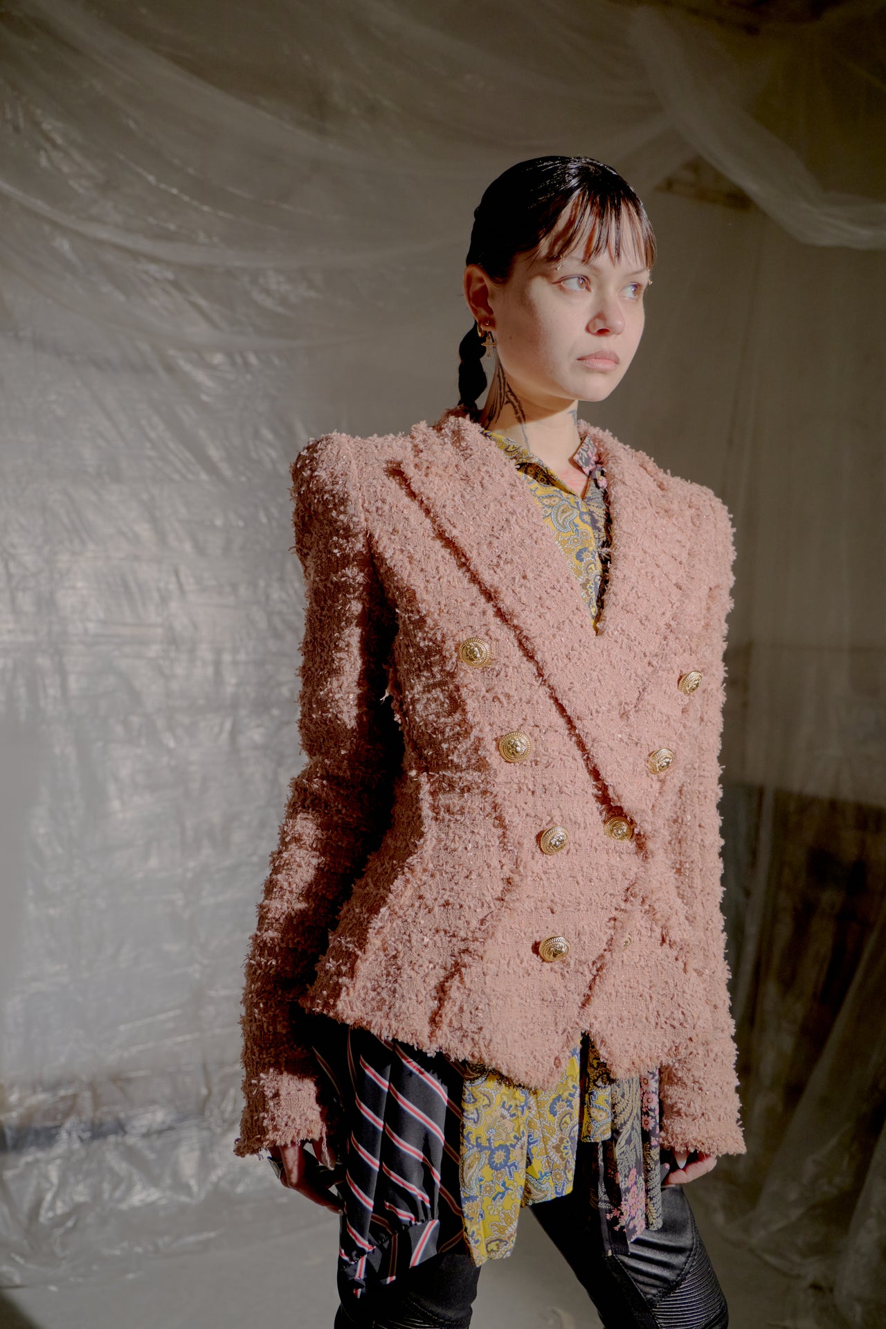 Person wearing a pink textured Balmain Double Breasted Tweed jacket and black high-heeled boots in a softly lit room.