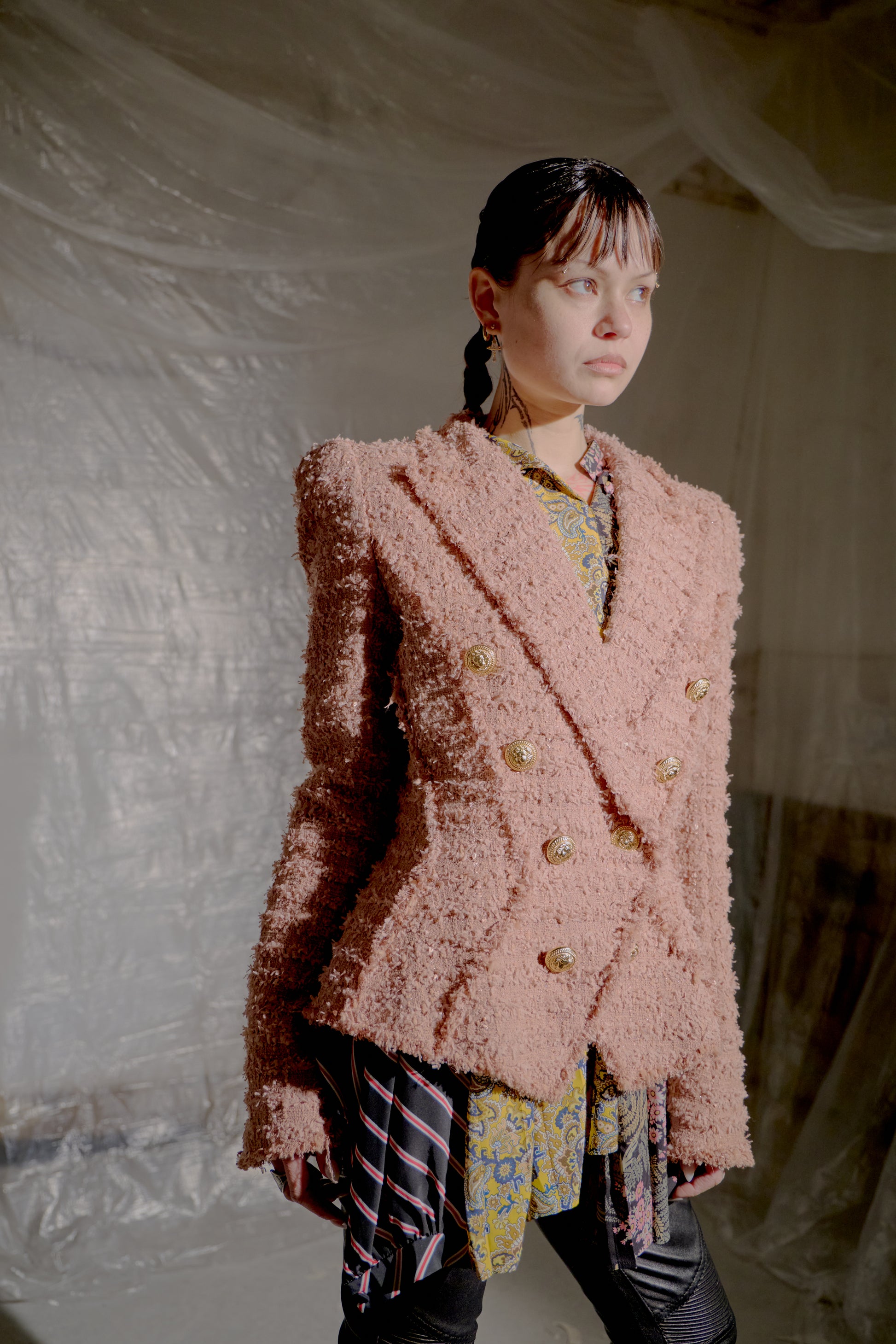 Person wearing a textured pink Balmain blazer in a softly lit indoor setting