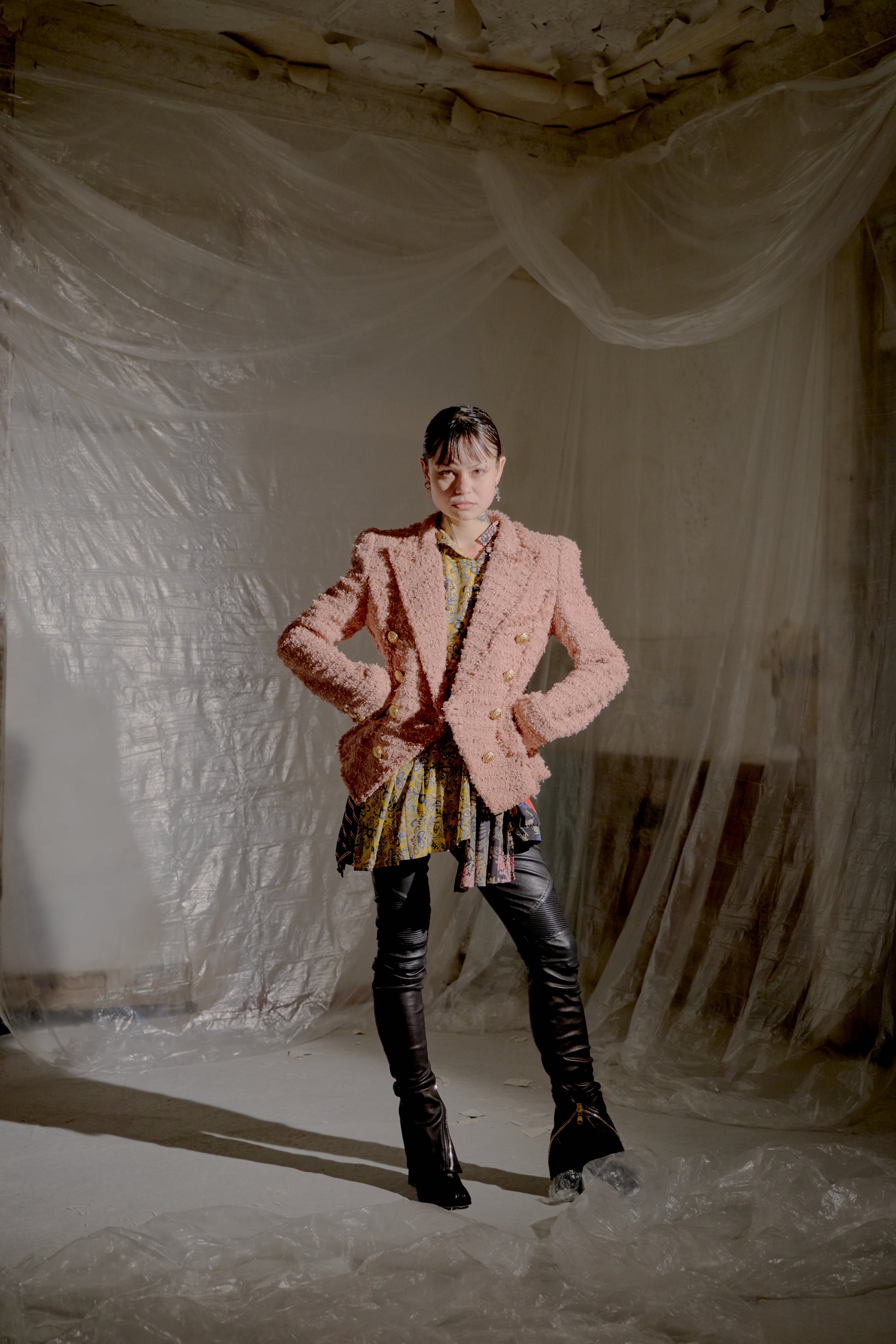 Person wearing a pink Balmain blazer and black pants standing in a room with white plastic sheeting.