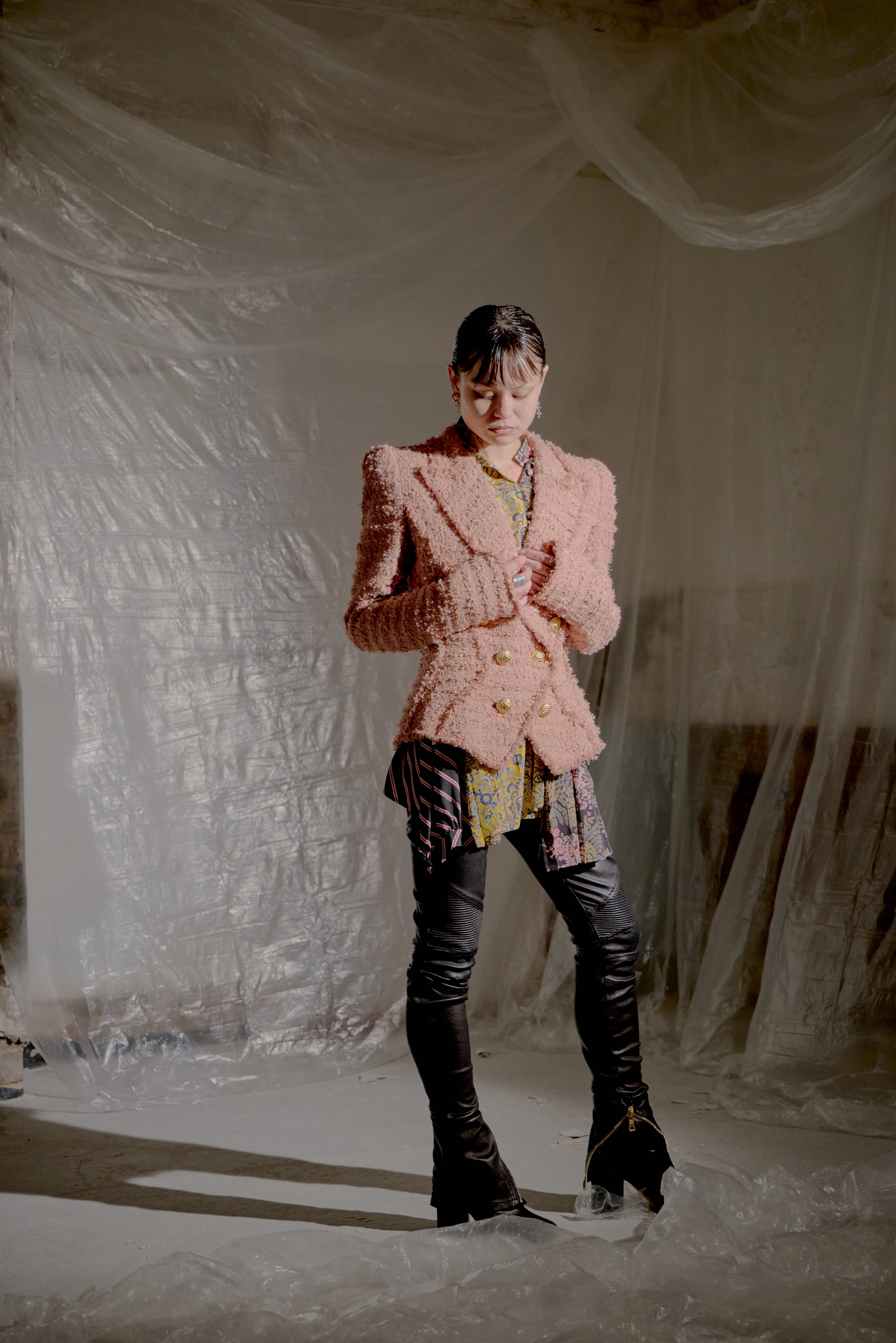 Person wearing a pink textured Balmain jacket and black pants standing against a white draped background