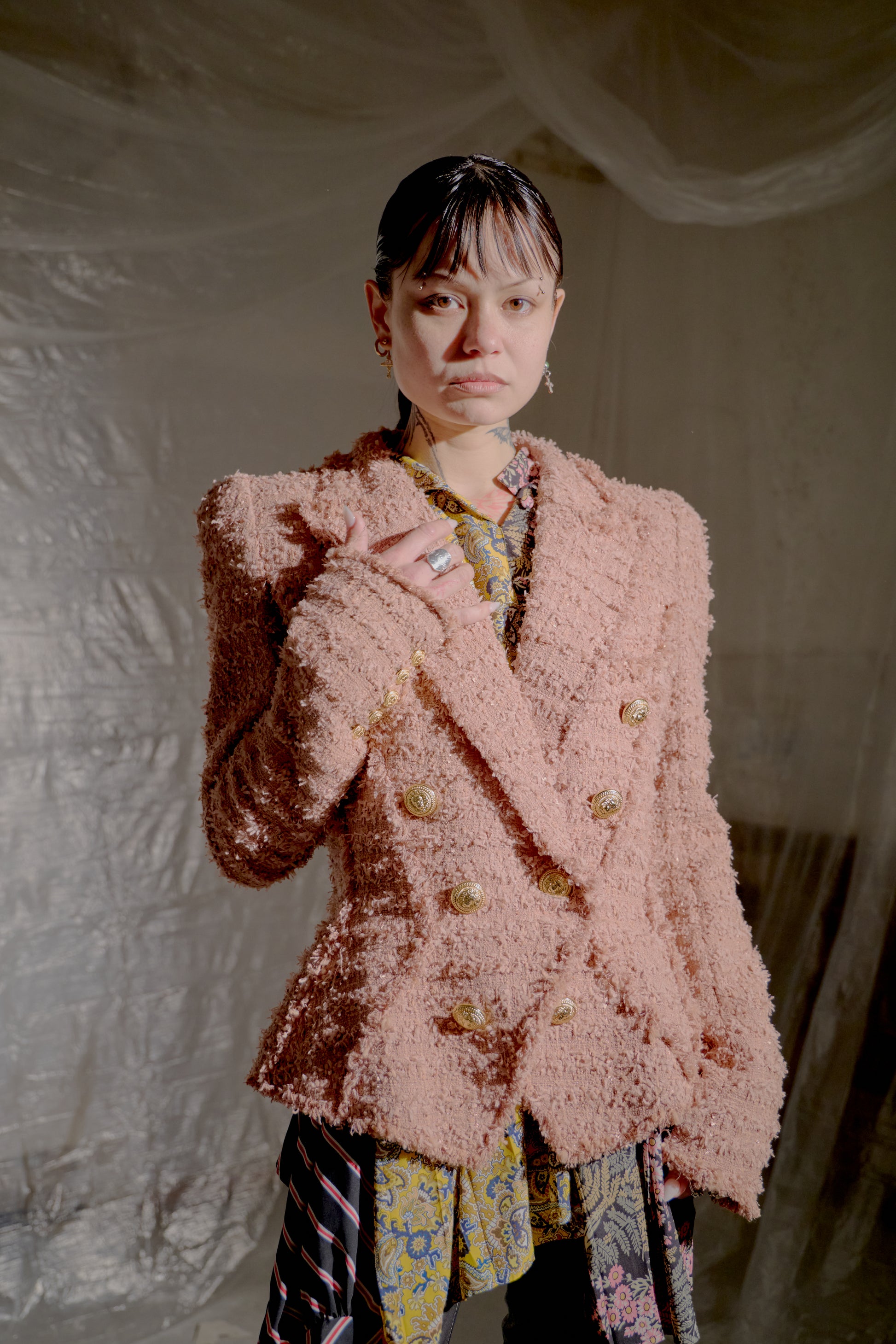 Person wearing a textured pink Balmain jacket with a patterned outfit against a textured white wall.
