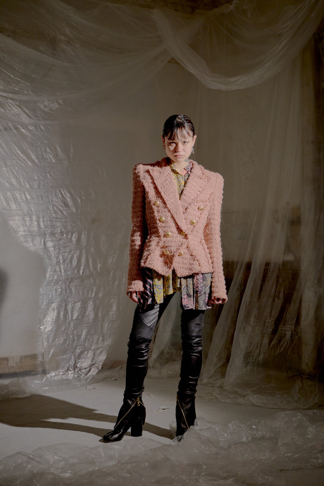 Person wearing a pink textured Balmain Double Breasted Tweed jacket and black high-heeled boots in a softly lit room.