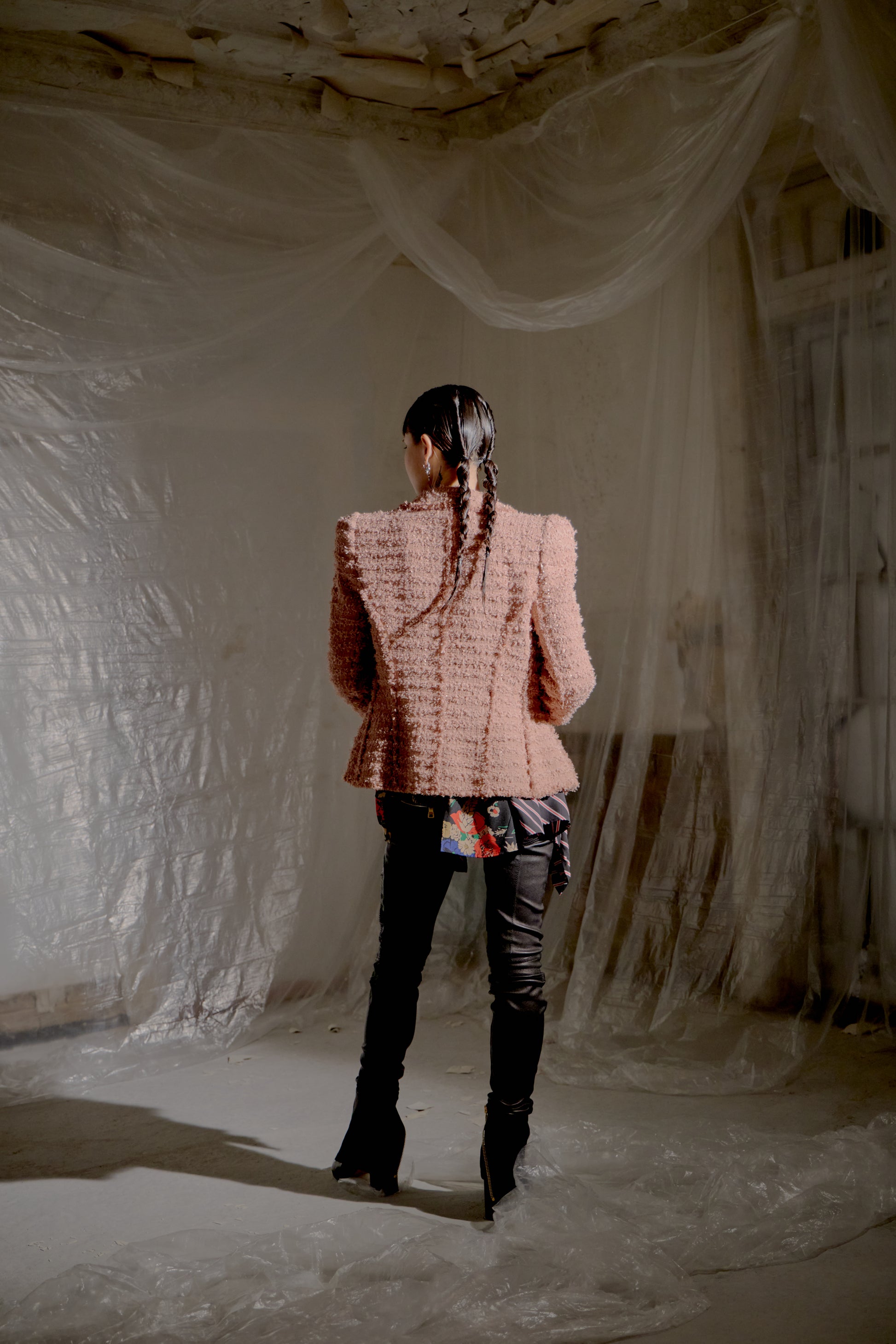 Person wearing a textured pink Balmain jacket and black pants standing in a room with draped fabric.