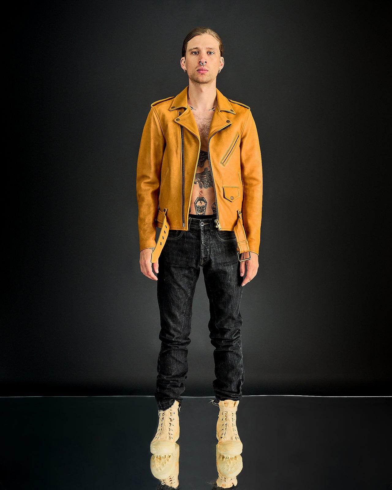 A person wearing a yellow leather Blackmeans biker jacket with a mid-rise design and long sleeves. The jacket features a front buckle detail and appears to be made of soft Japanese cowhide.