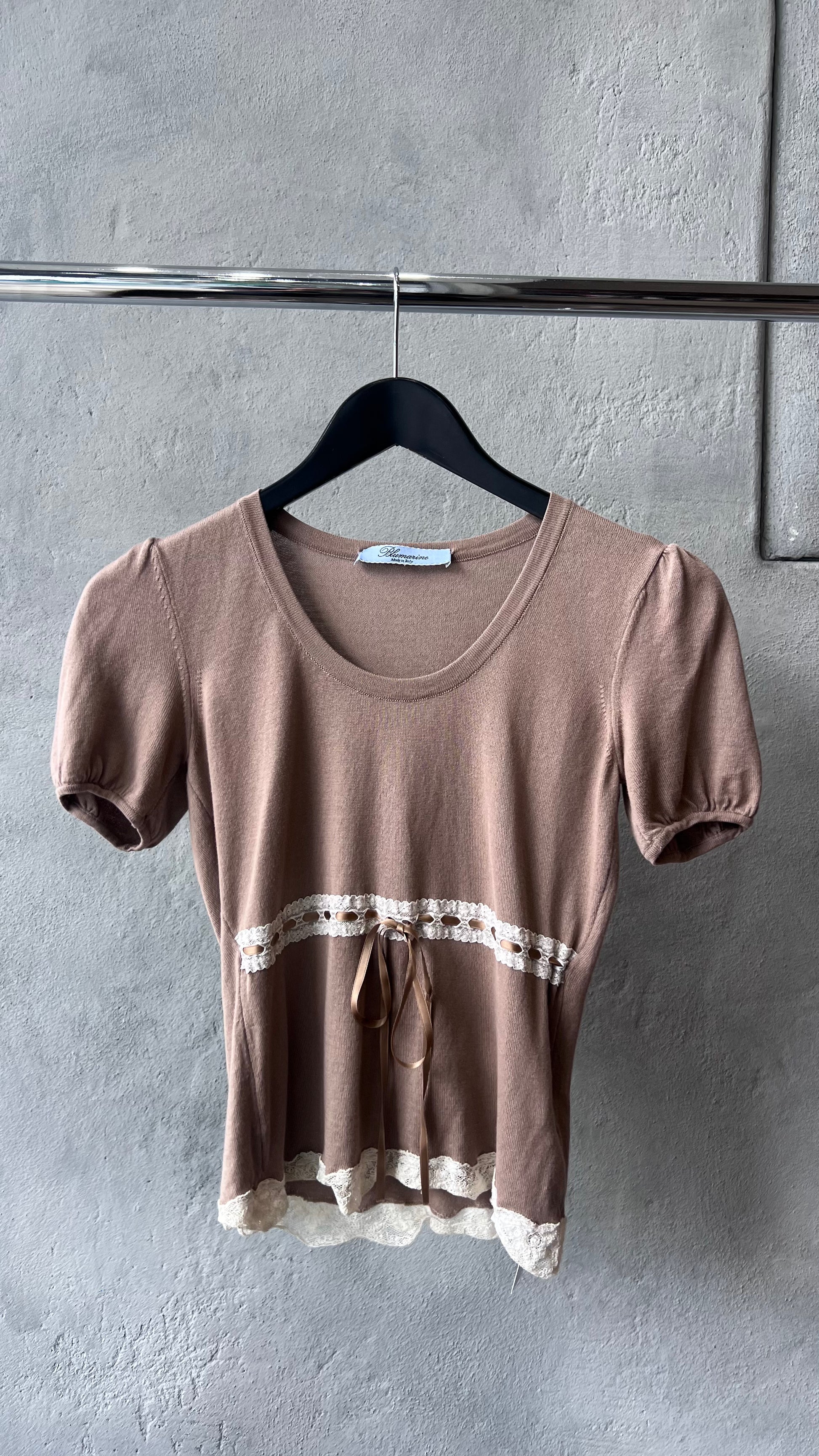Brown short-sleeve Blumarine top with lace trim on a hanger against a gray wall.