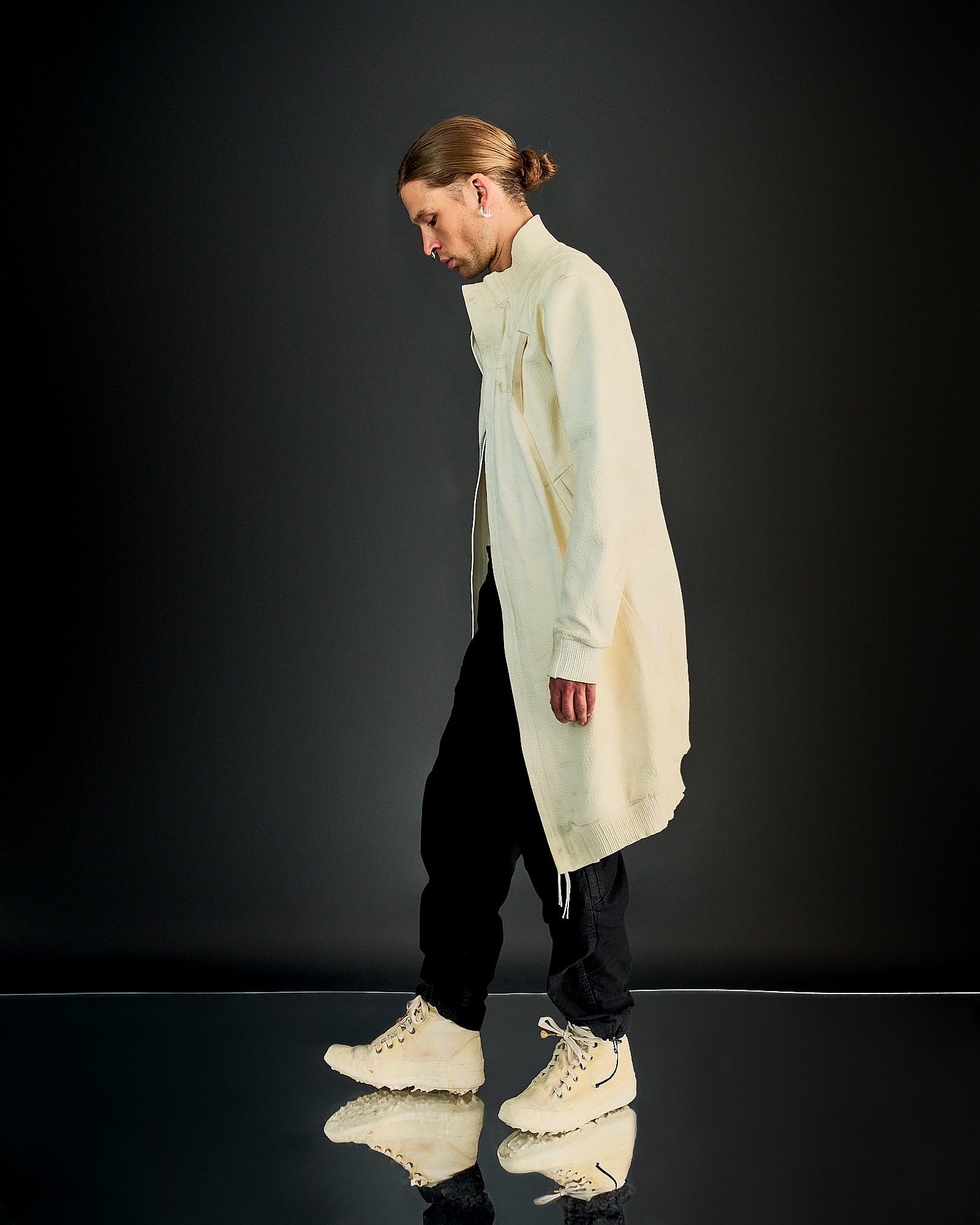 Person in cream-coloured long knit Boris Bidjan Saberi jacket, black pants, and off-white high-top sneakers. Fashion-forward style with a modern, minimalist aesthetic.