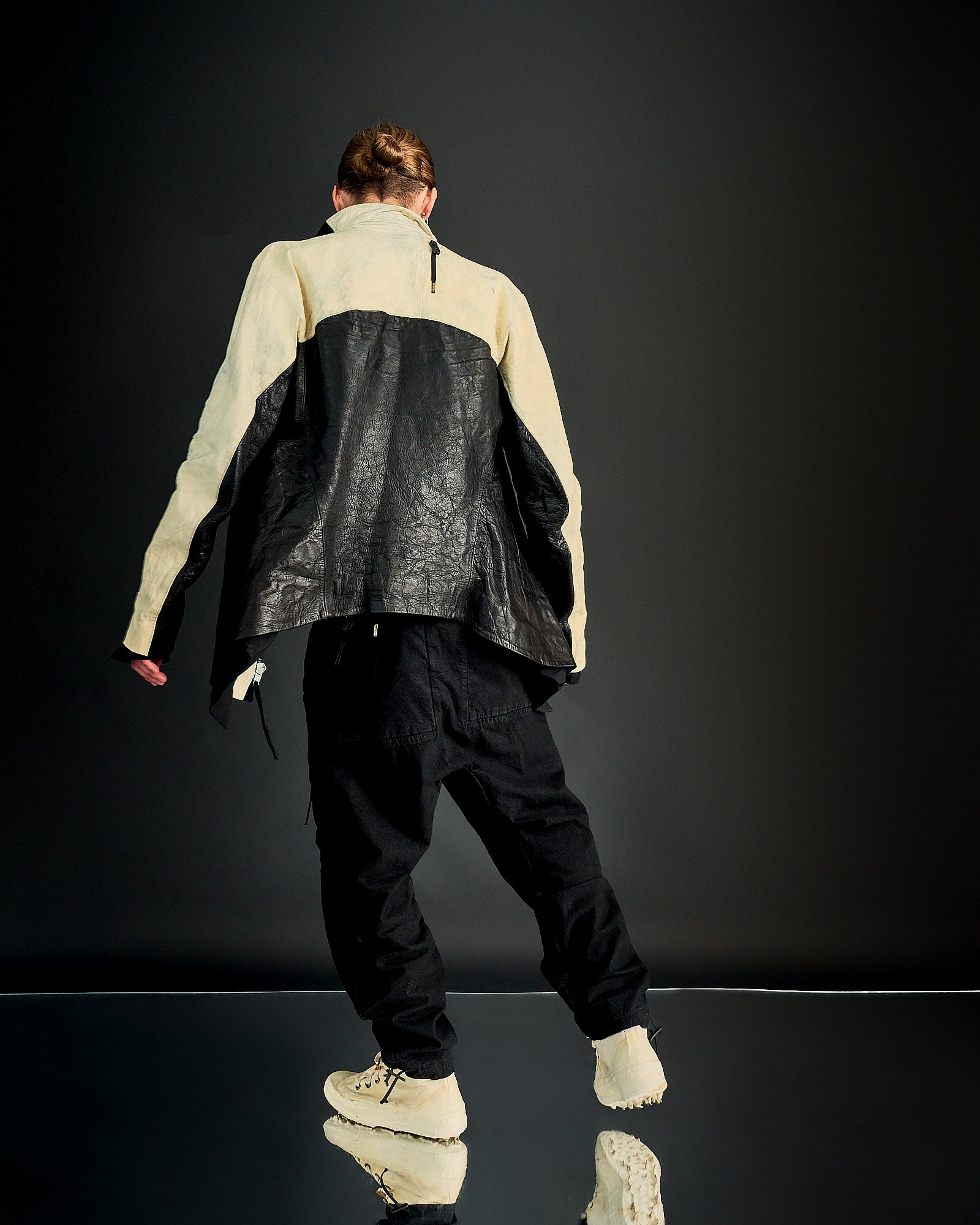 A person wearing a longline zip-up Boris Bidjan Saberi jacket with crumpled buckskin deerhide leather, featuring a double-zip front and a silver-aglet lace detail on the back.