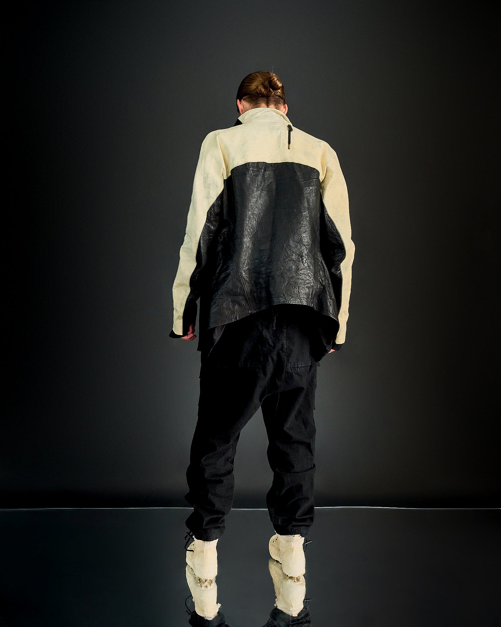 A person stands against a dark background wearing a black and beige Boris Bidjan Saberi outfit.
