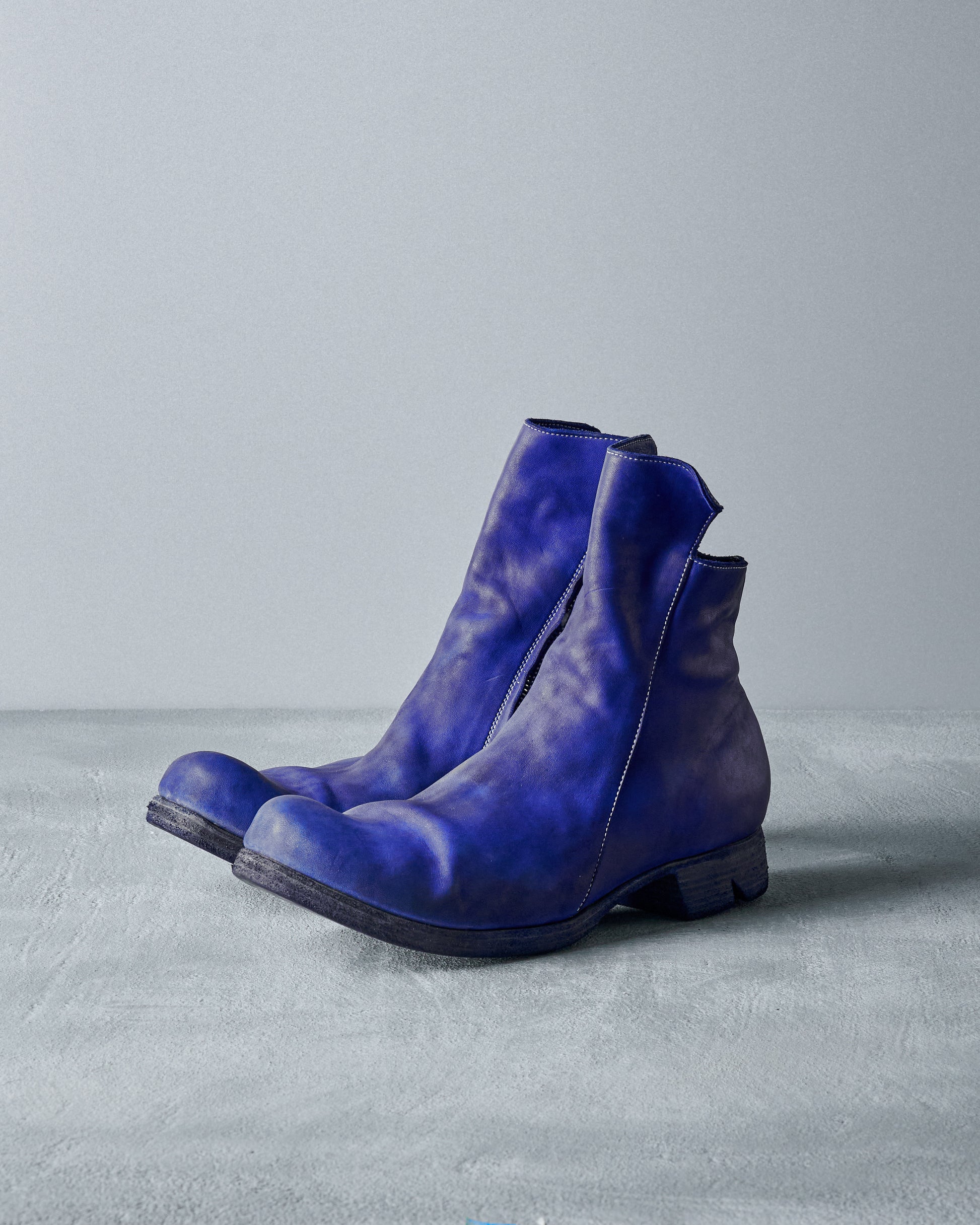 A pair of worn blue leather Boris Bidjan Saberi boots with visible scuff marks sits on a textured grey surface.