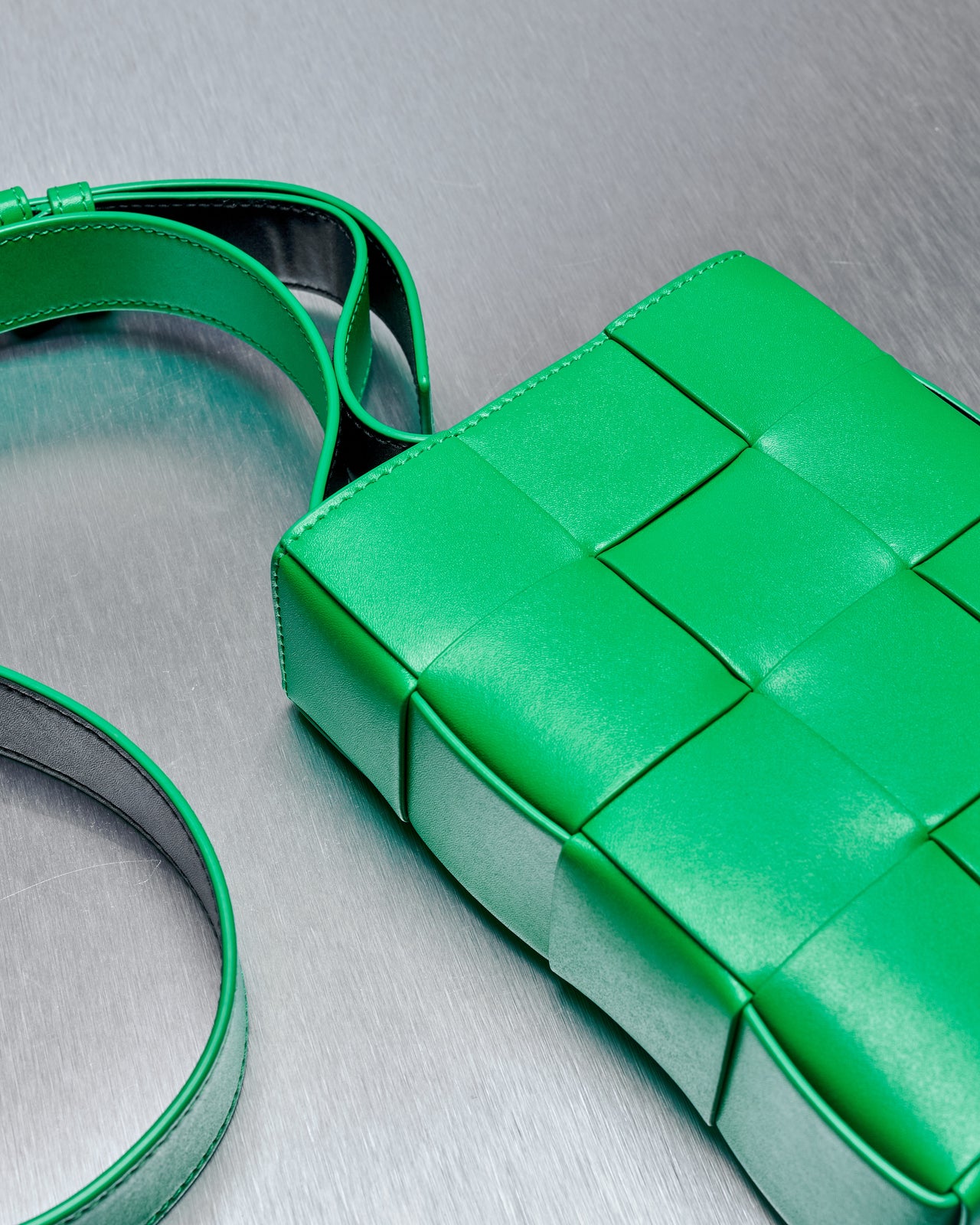 A green woven intrecciato leather shoulder bag with adjustable straps and a magnetic tab closure.