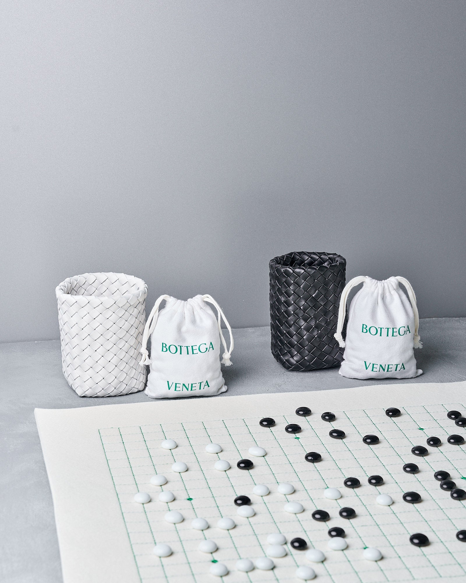 Three Bottega Veneta bags and a Go board with pieces on a gray surface.