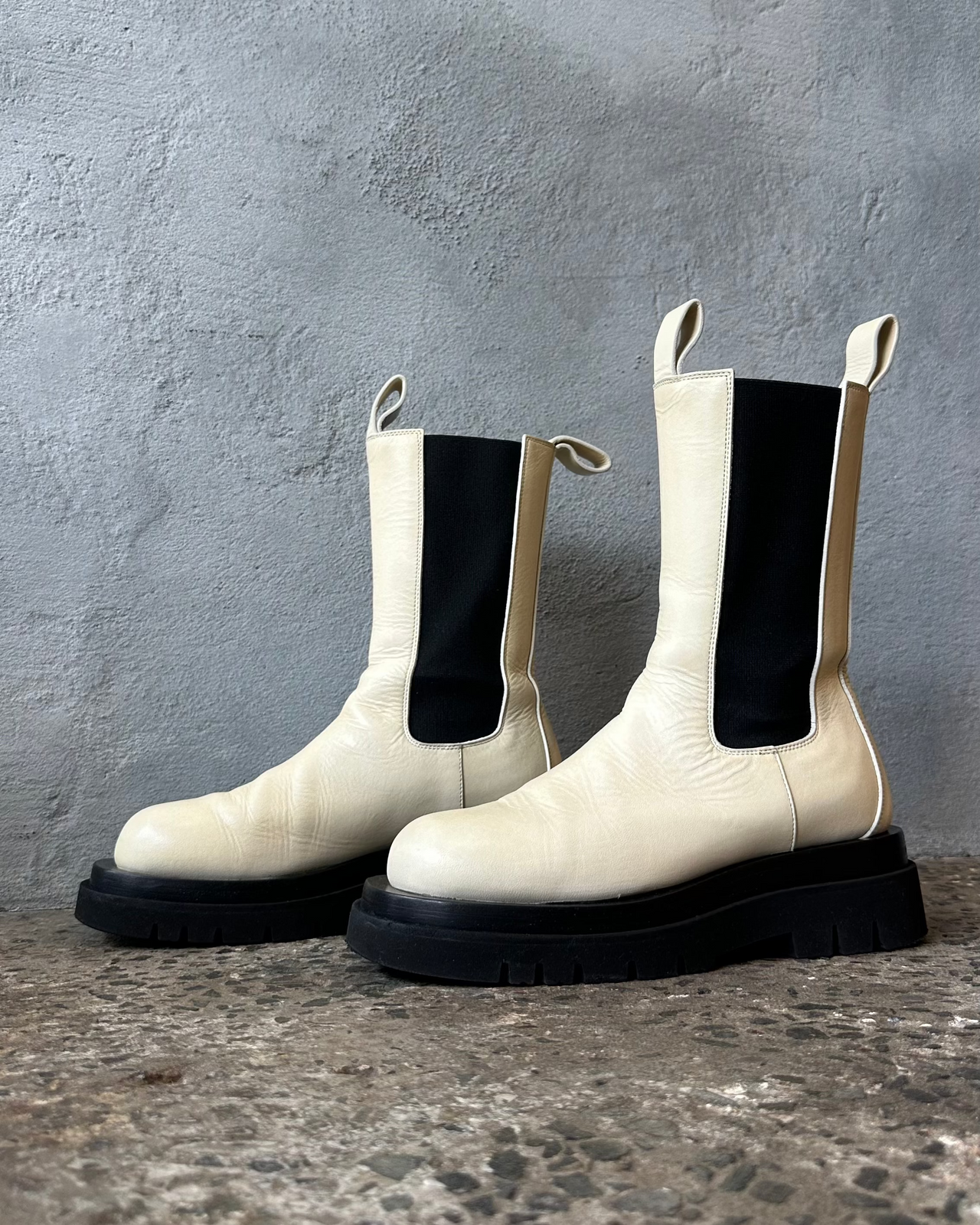 White Bottega Veneta Chelsea boot with black sole on a gray surface against a gray background