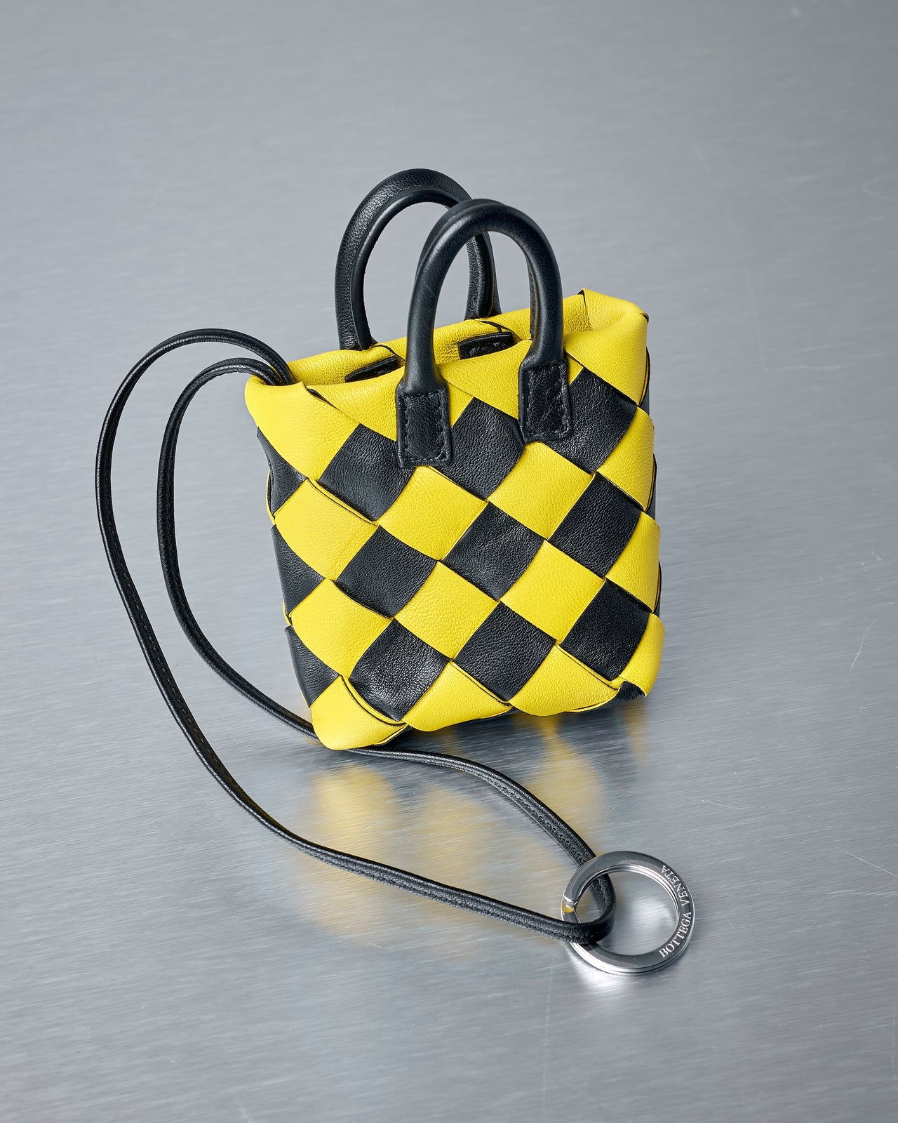 Yellow and black checkered Bottega Veneta bag charm with a strap on a gray background