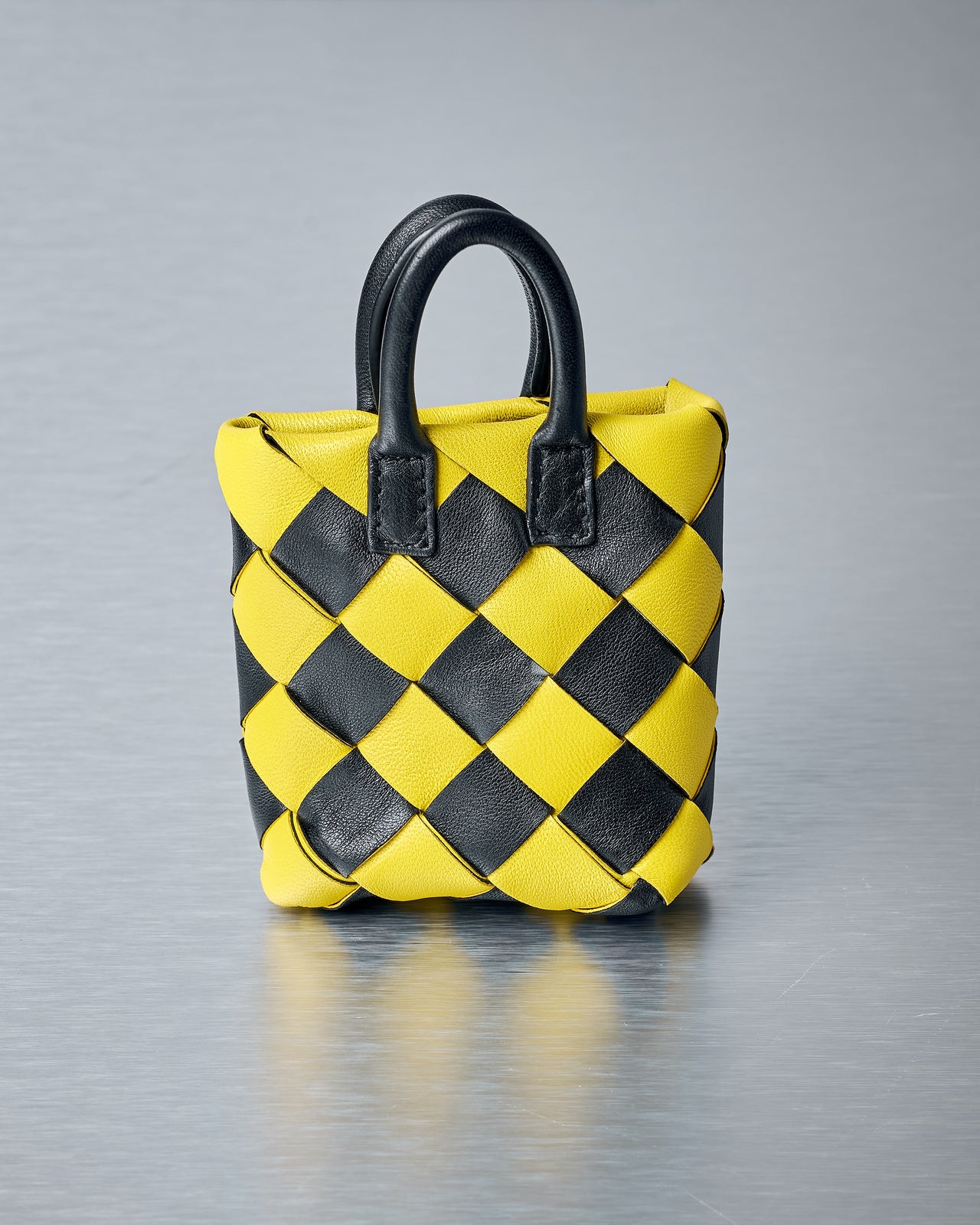 Yellow and black checkered Bottega Veneta bag charm with a strap on a gray background